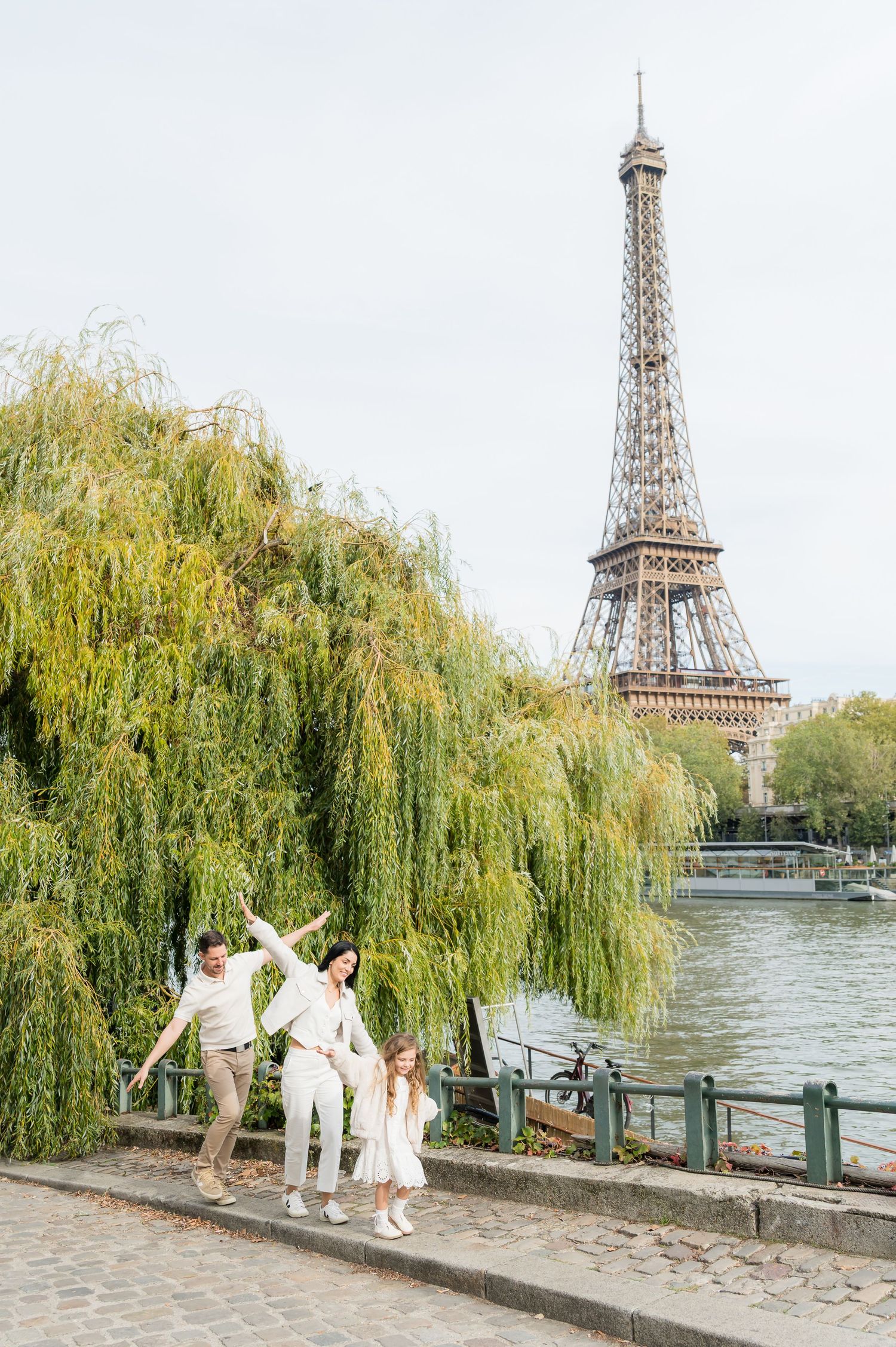 A sequence of joyful poses by people in white clothing along the Seine River with the Eiffel Tower in view.