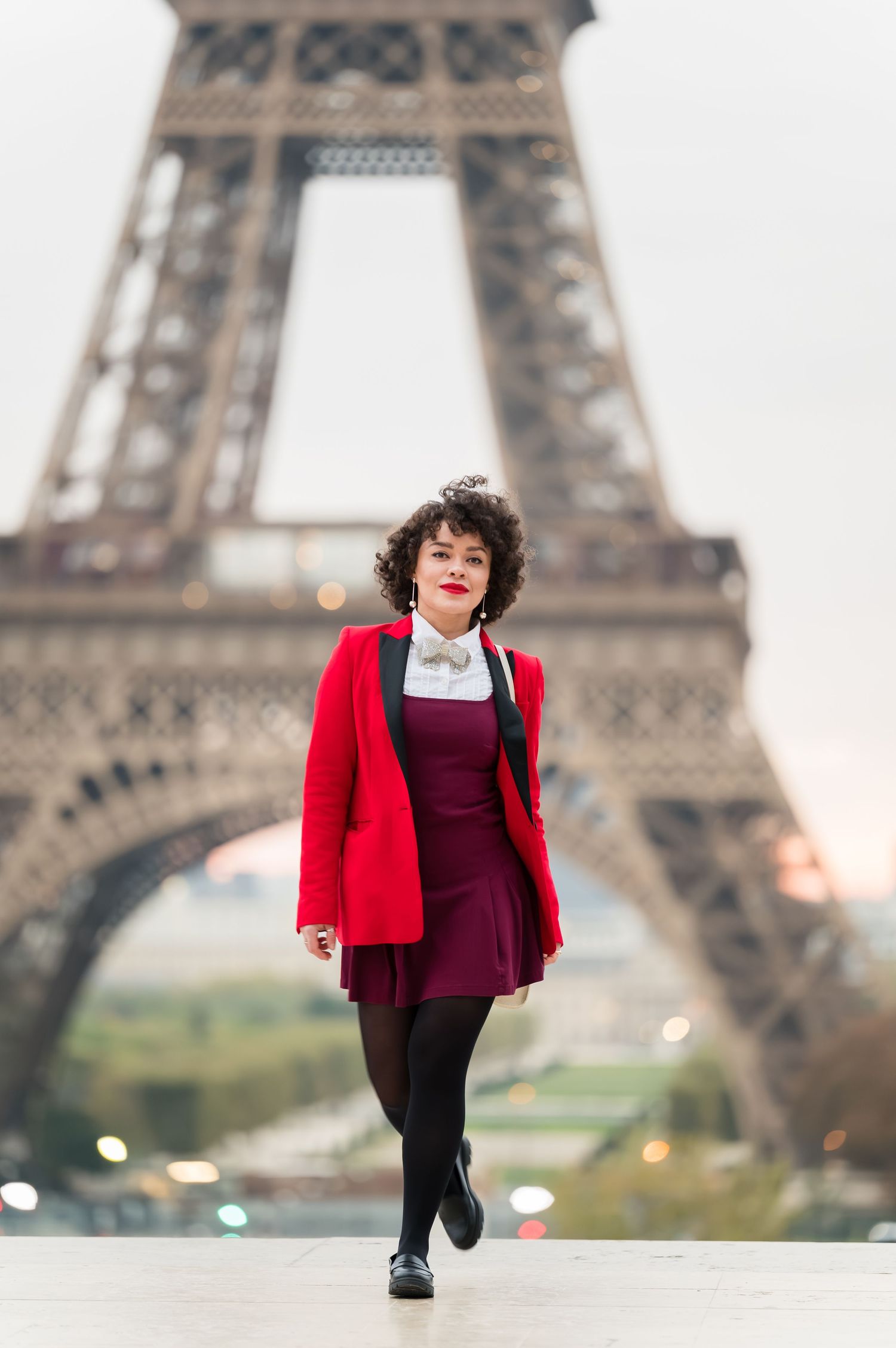 A child in a red jacket and burgundy dress walks in front of the iconic Eiffel Tower in Paris.