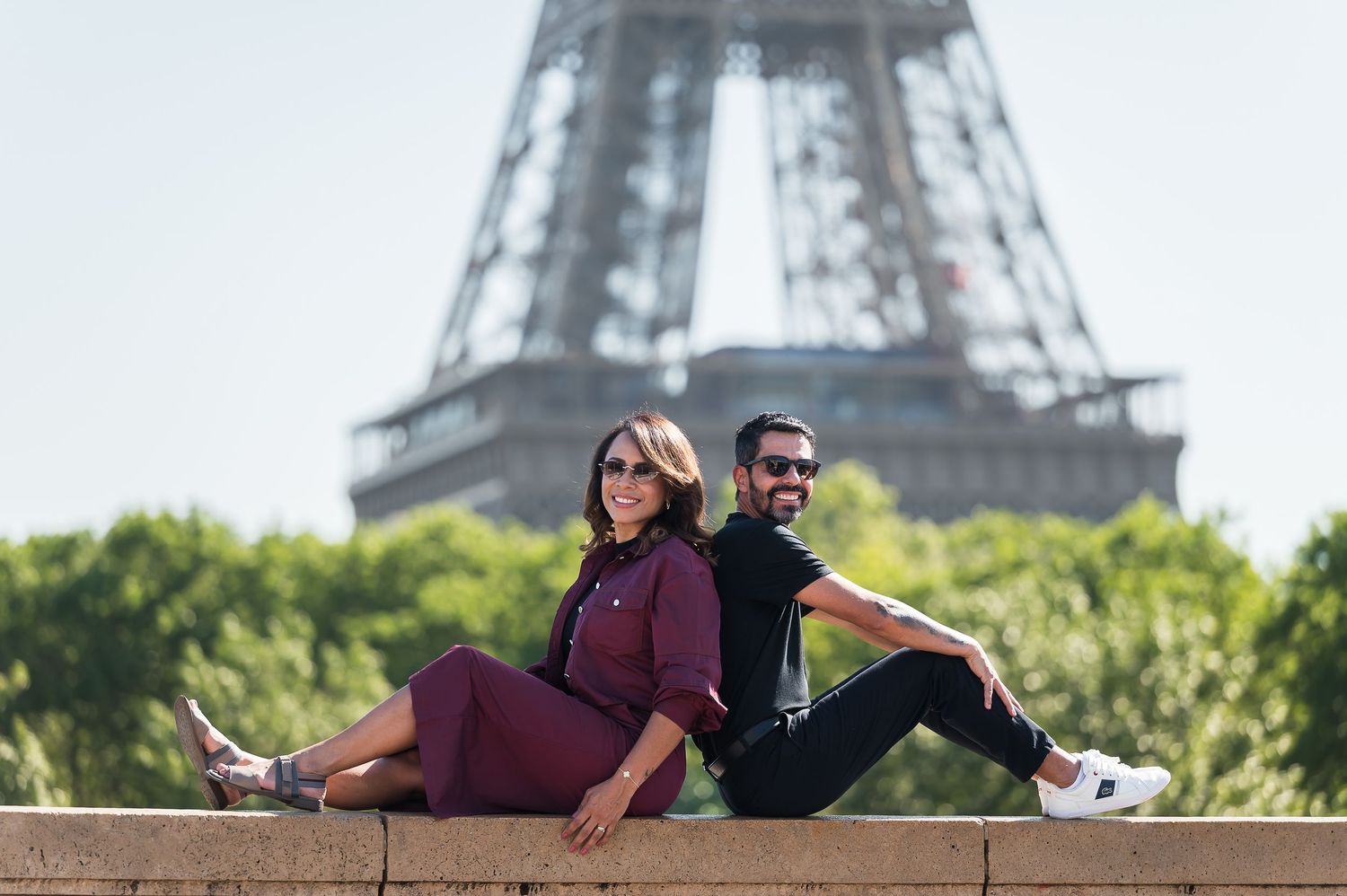 Couple sitting back-to-back on stone steps with the Eiffel Tower in Paris, France in the background.