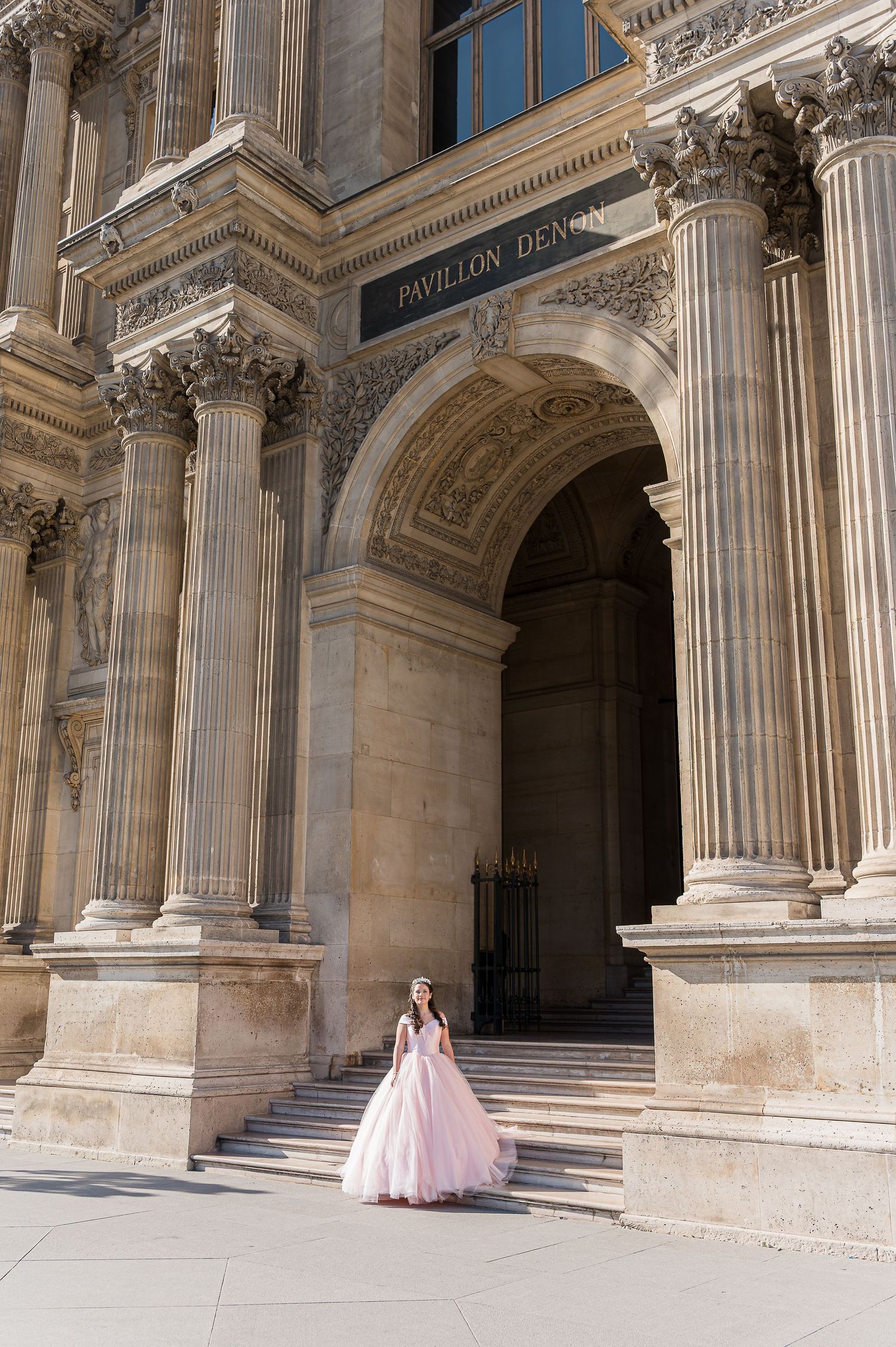 Woman in pink ball gown poses on steps of ornate Pavillon Denon at the Louvre in Paris.