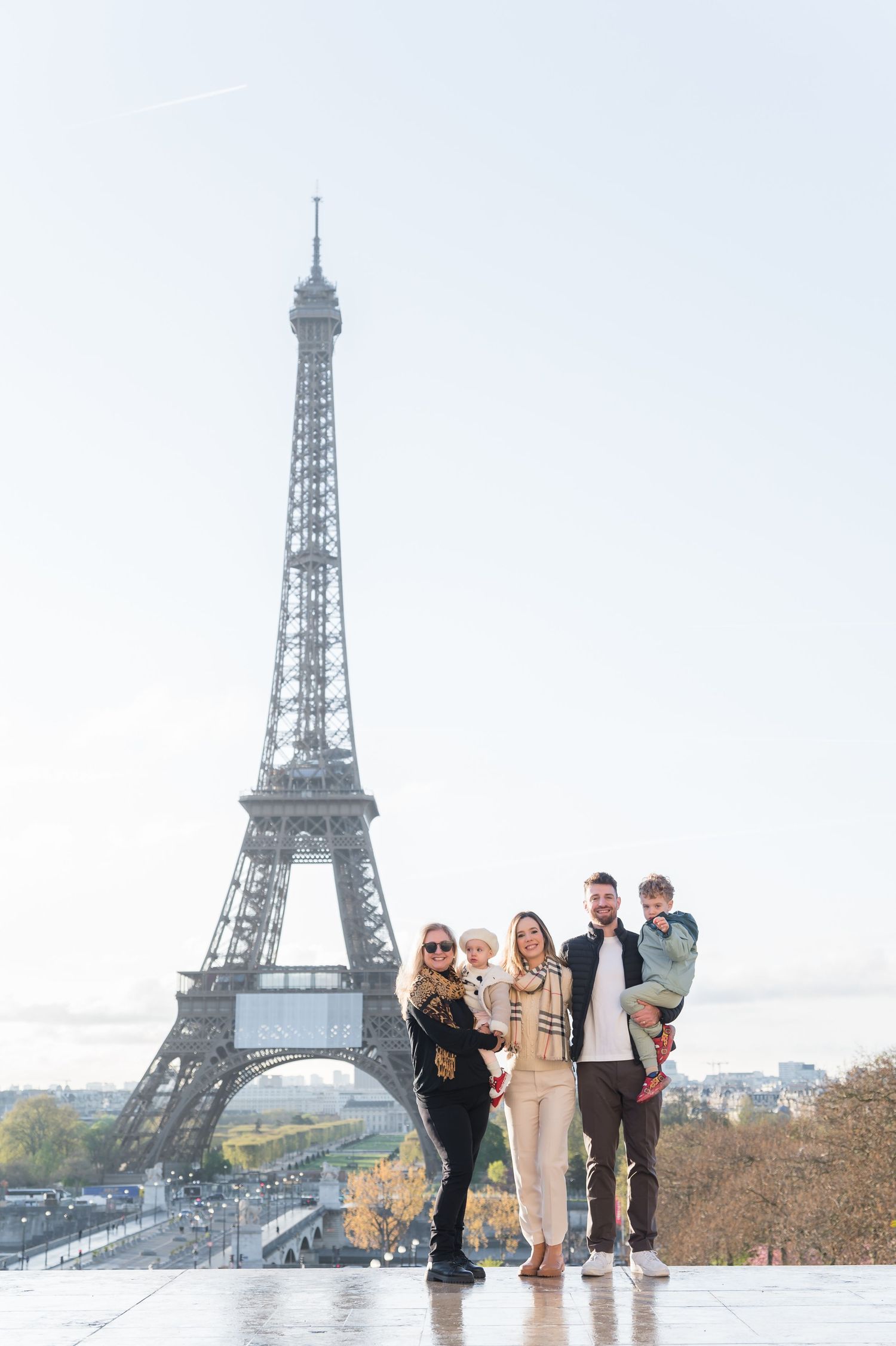 Family of four posing happily in front of the Eiffel Tower in Paris on a clear autumn day.