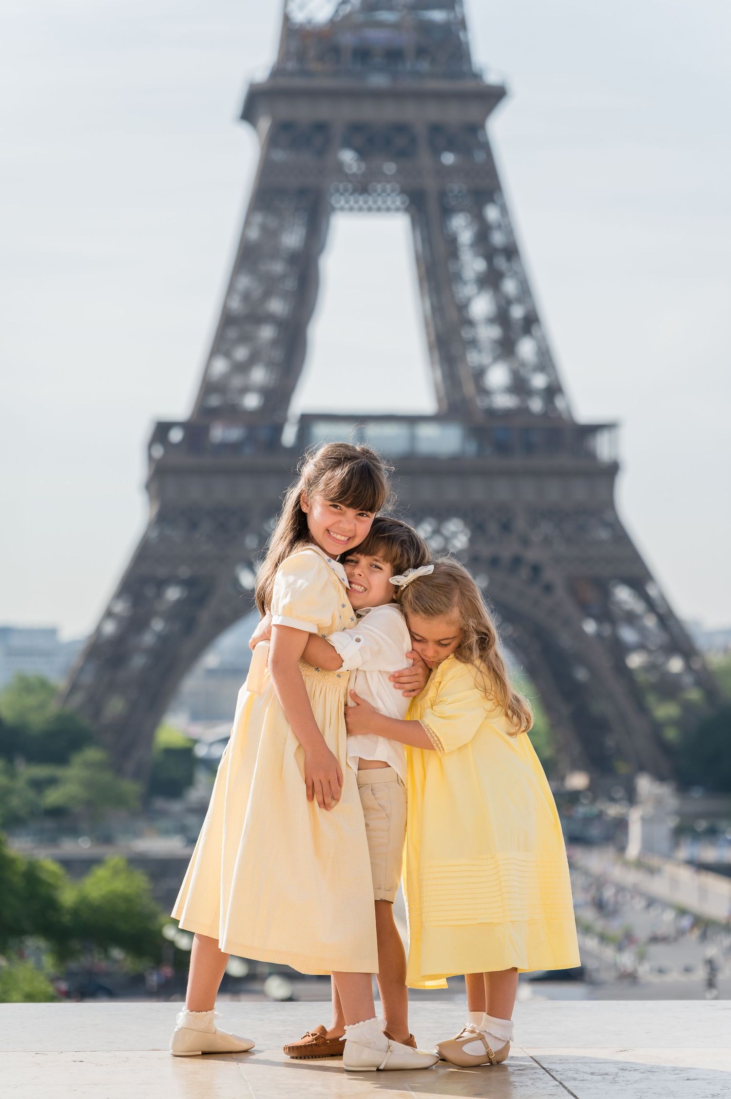 Children in matching yellow dresses playfully pose at different angles with the Eiffel Tower in the background of Paris.