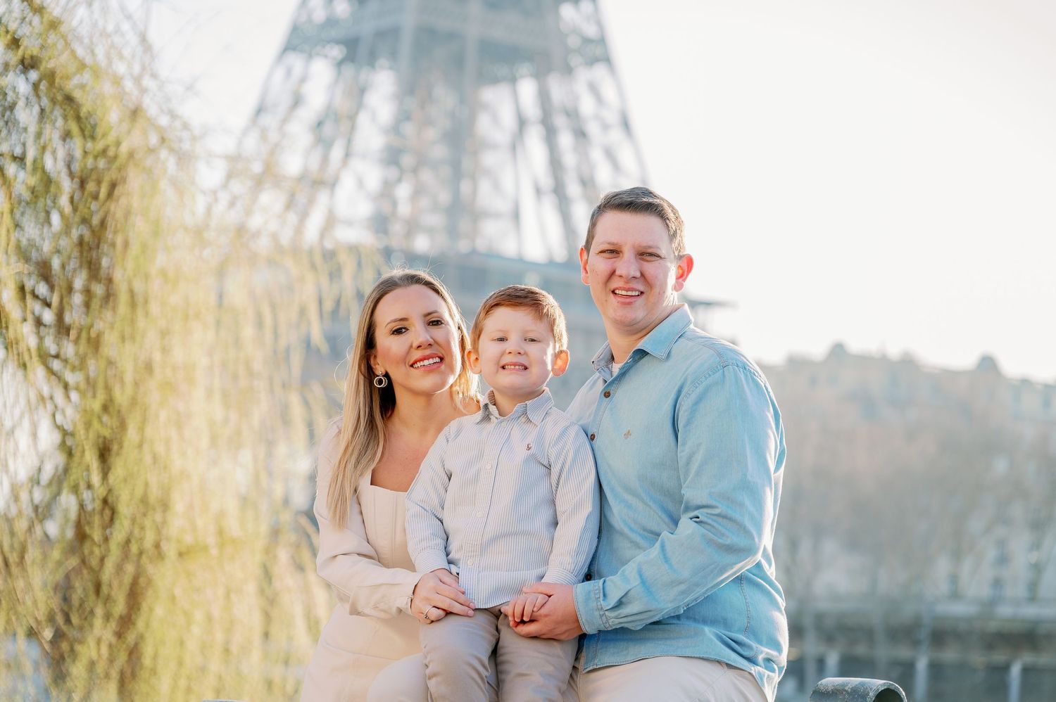 A family poses together in front of the Eiffel Tower on a sunny day in Paris.