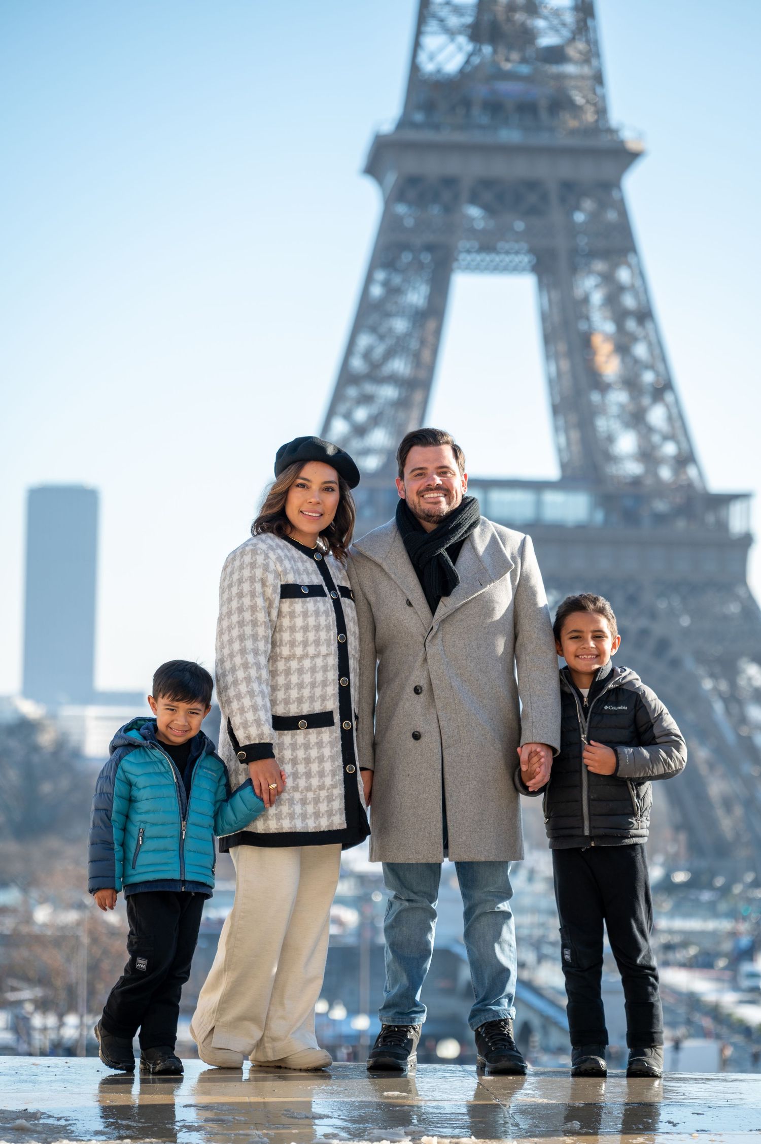 A family poses together in winter coats with the iconic Eiffel Tower rising behind them in Paris.