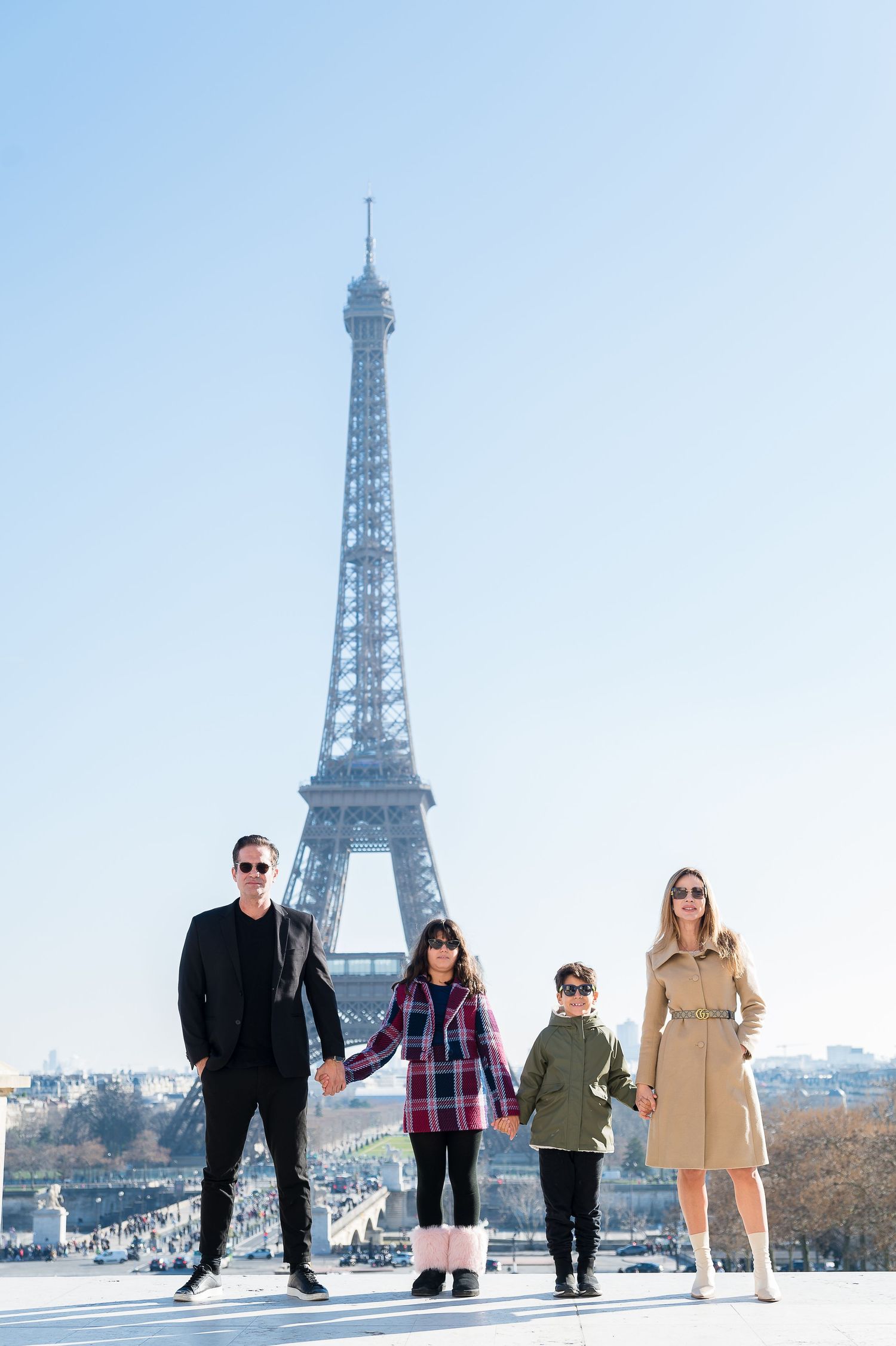 Four people stand in a line against the backdrop of the Eiffel Tower on a clear winter day in Paris.