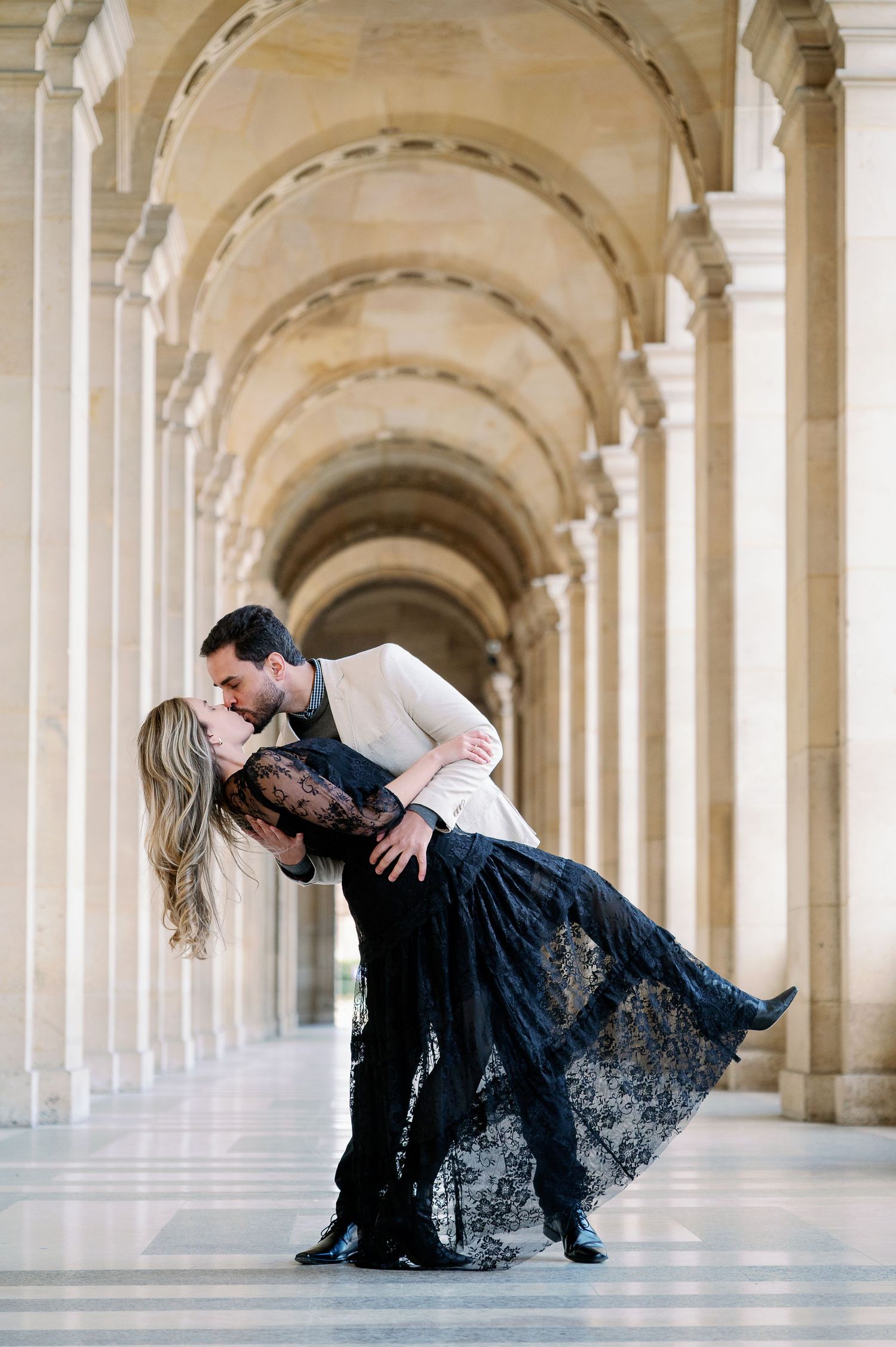 A romantic dance pose in an elegant colonnade hallway with arched architecture.