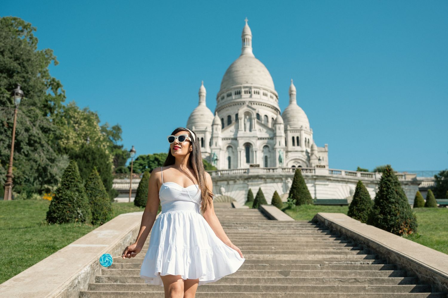 A scenic view of the white-domed Sacre-Coeur Basilica in Paris with tourists enjoying a sunny summer day on the steps.