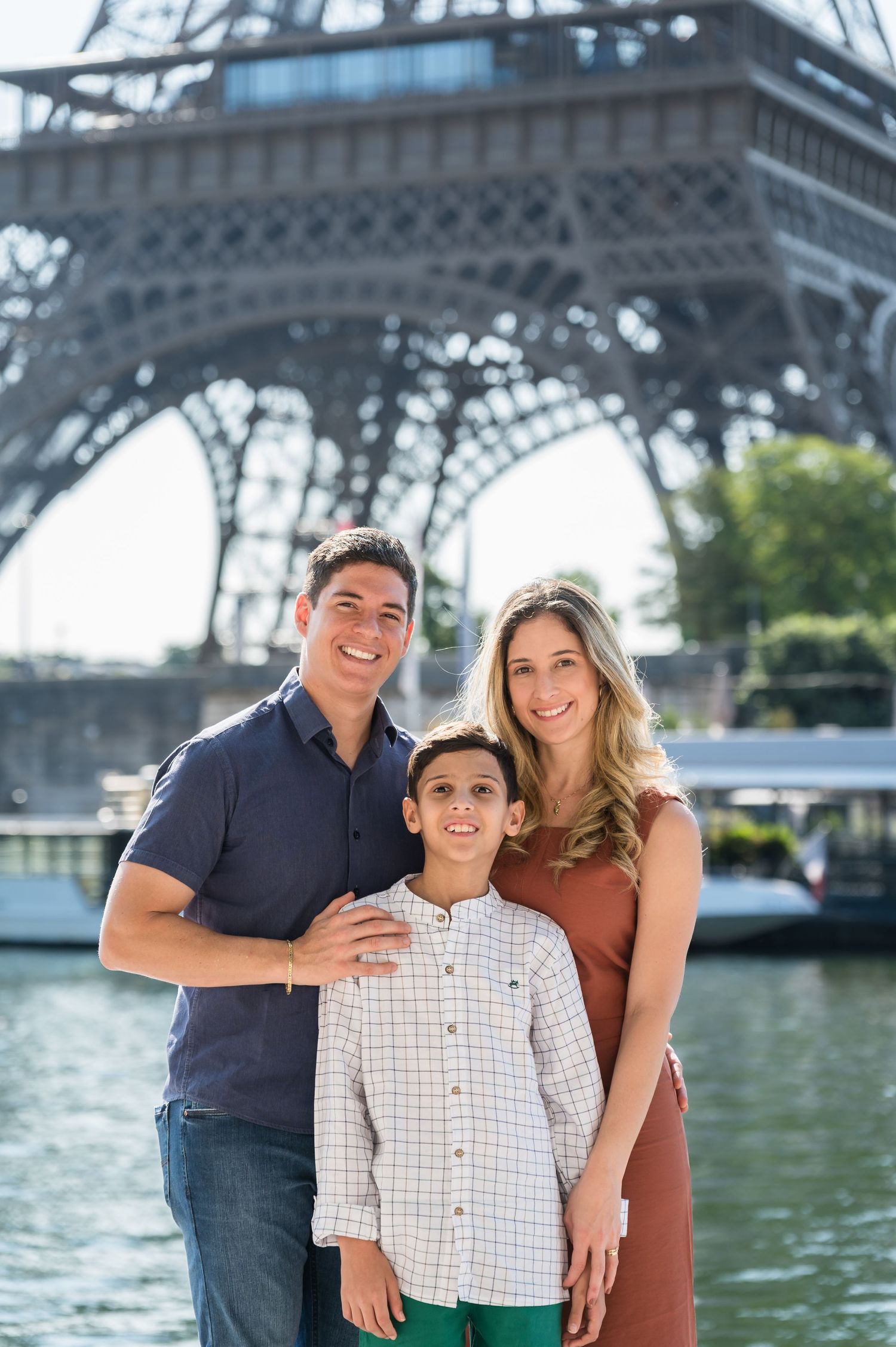 A family stands together for a photo in front of the Eiffel Tower on a sunny day in Paris.