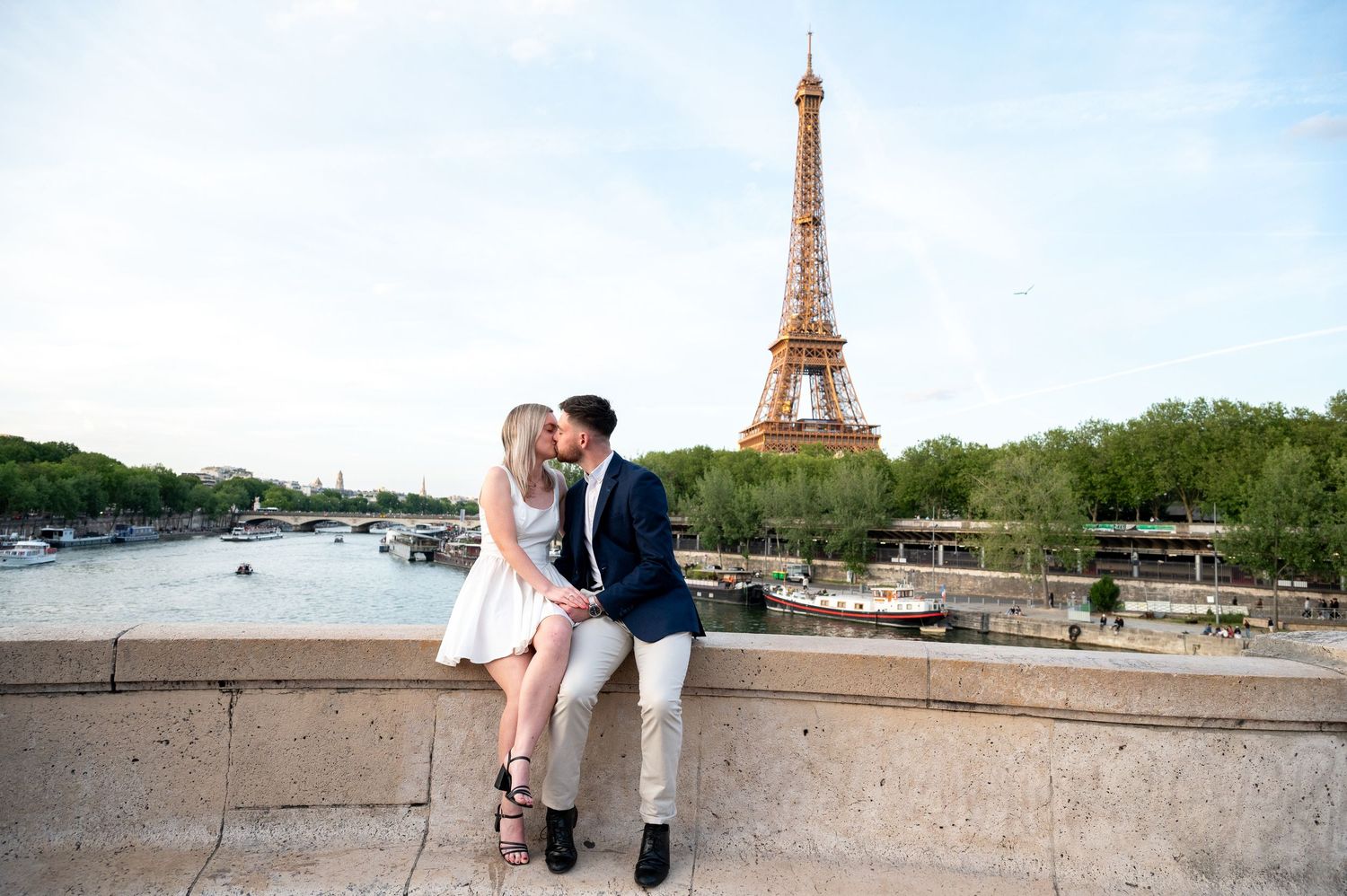 Romantic couple poses along a stone wall in front of the Eiffel Tower in Paris during sunset lighting.