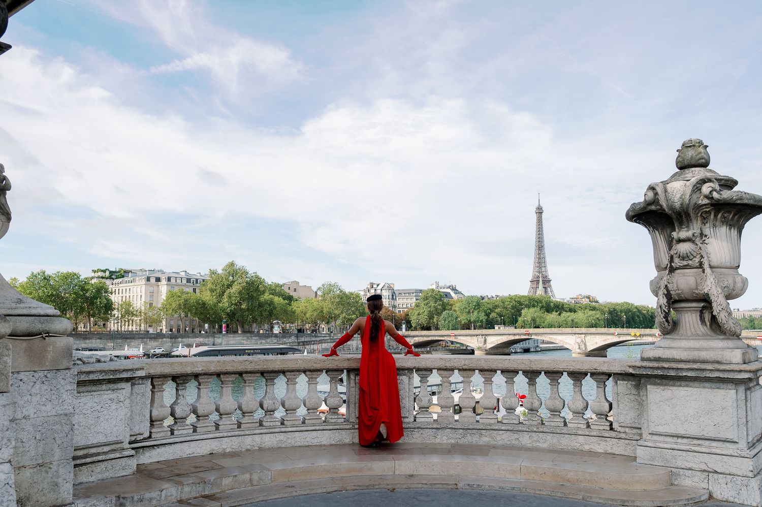 Woman in red dress poses on ornate Paris bridge with Eiffel Tower in background.