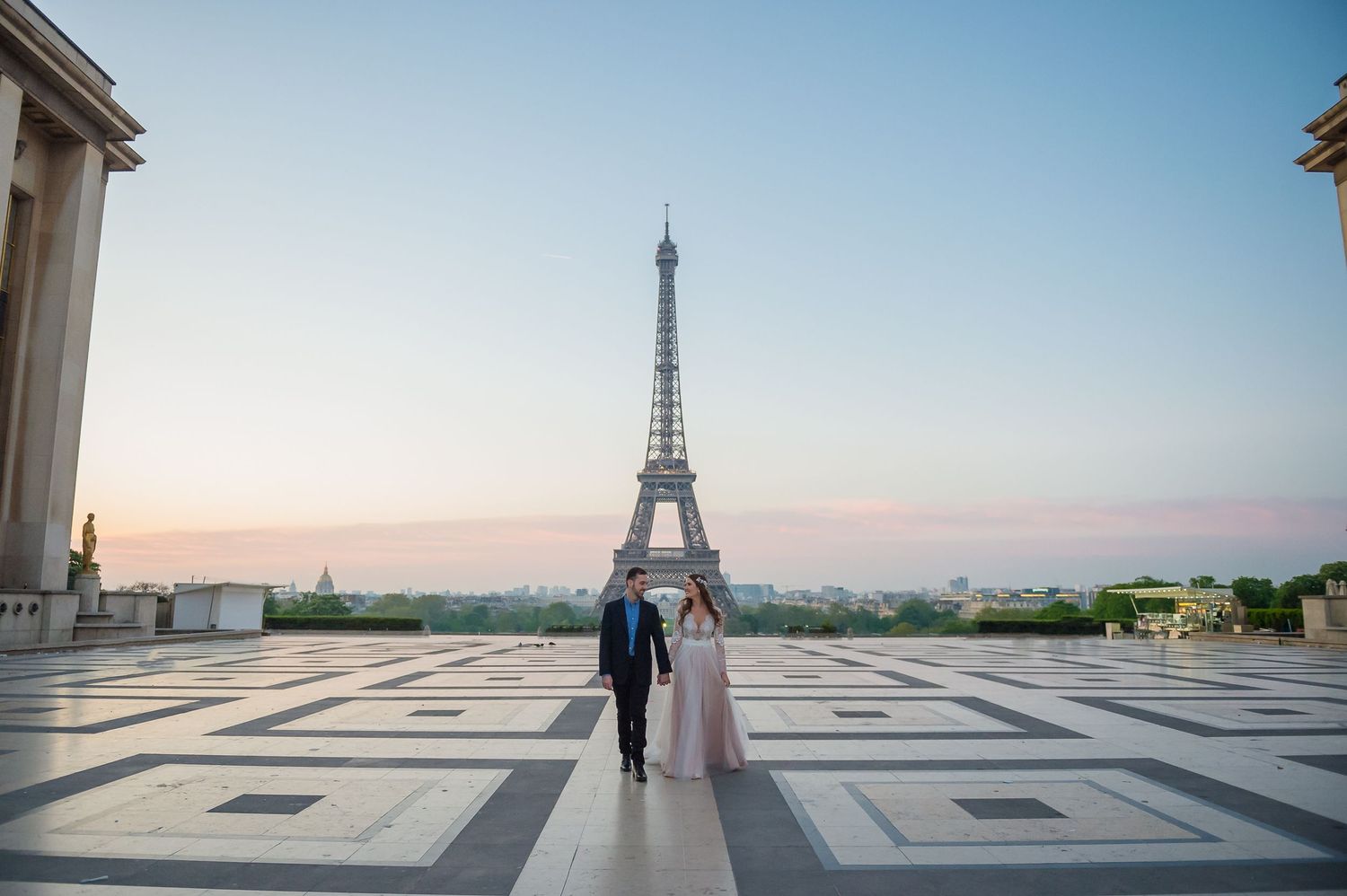 Couple walking towards Eiffel Tower on patterned plaza at sunset.