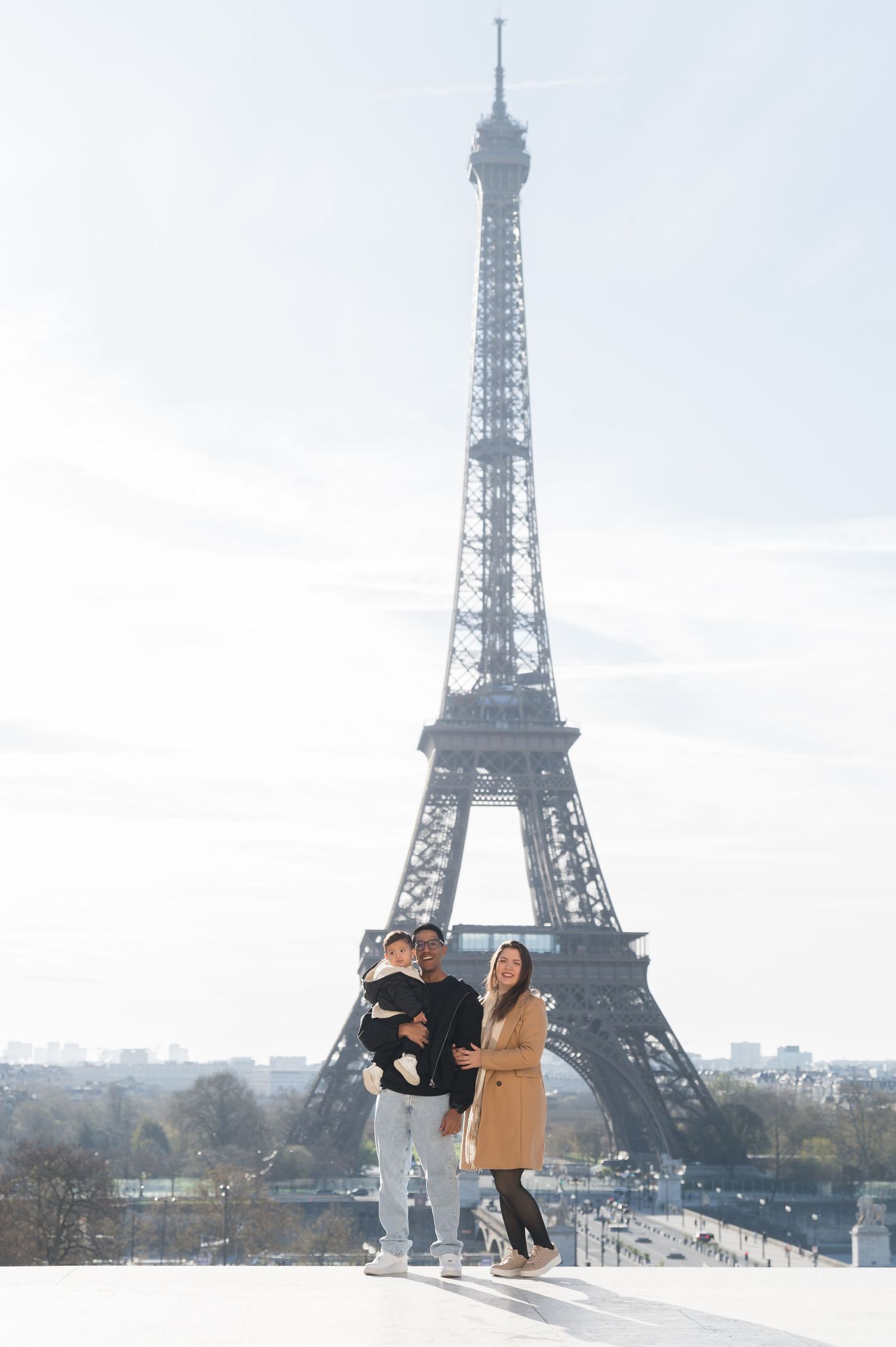Family posing in front of the Eiffel Tower in Paris on a sunny day.