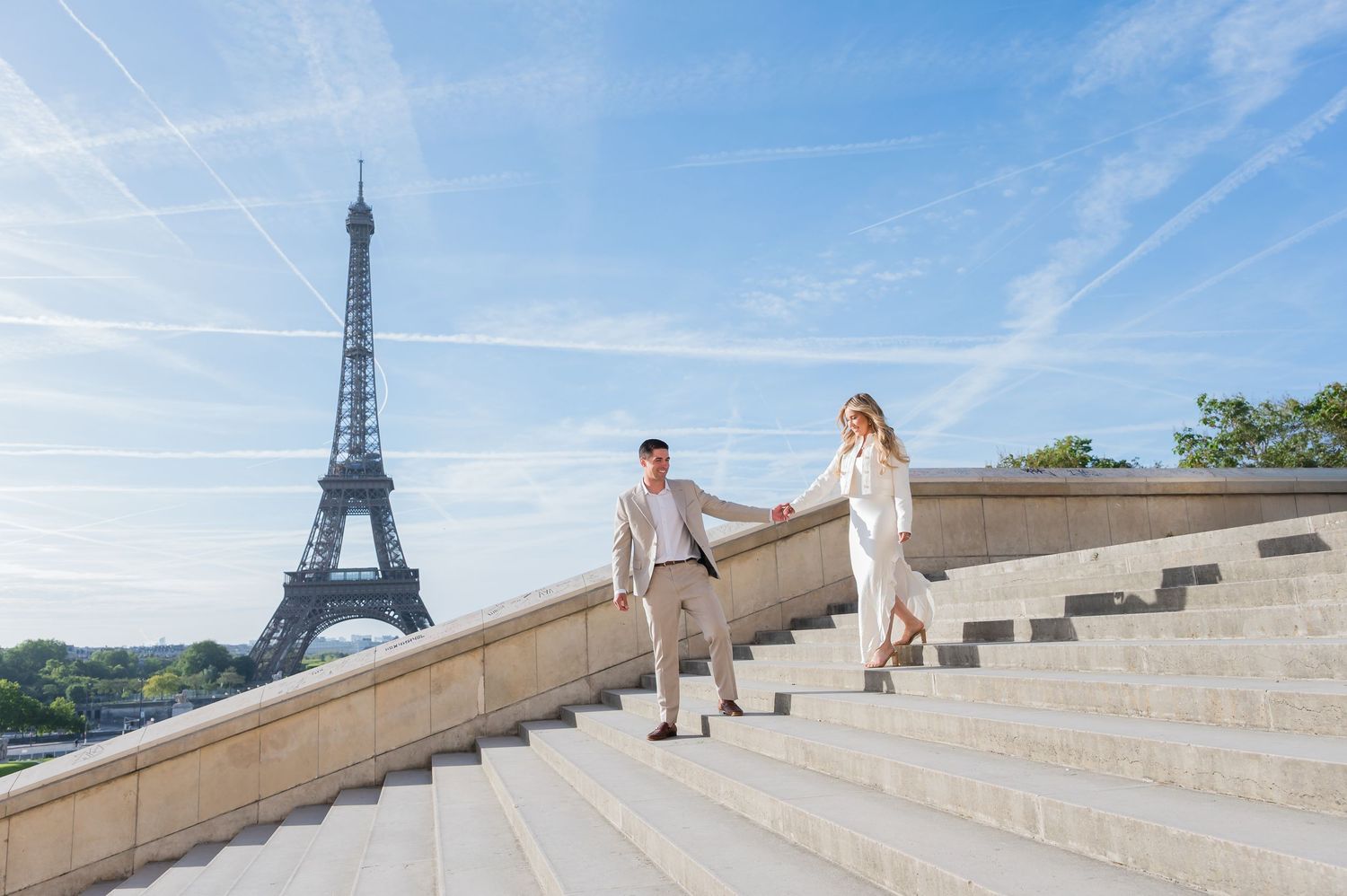 Two people walking up stone steps at Trocadero Square with the Eiffel Tower in the background on a sunny day in Paris.