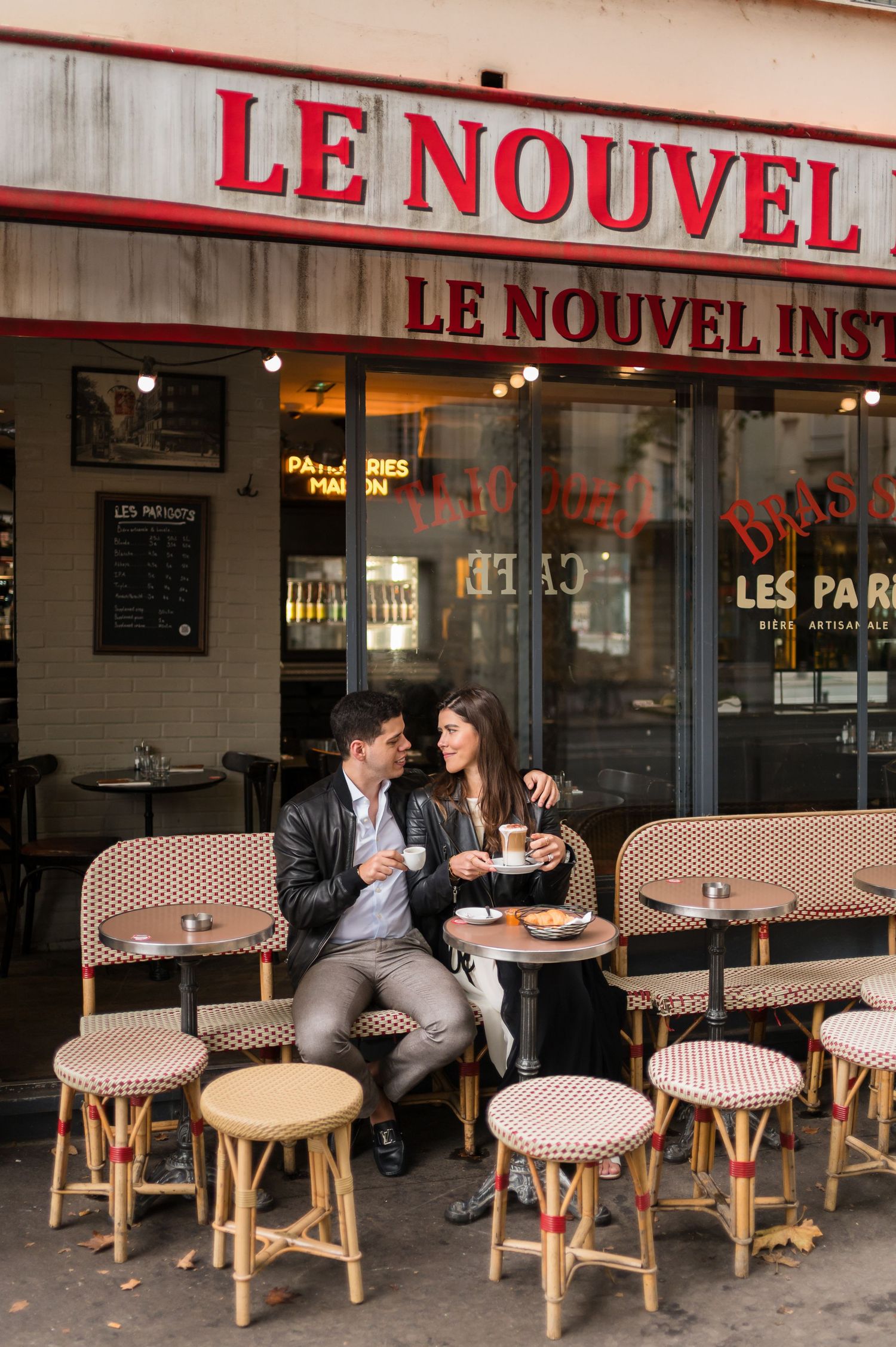 Couple enjoying coffee at Le Nouvel Institut cafe in Paris, sitting at a classic bistro table with wicker stools.