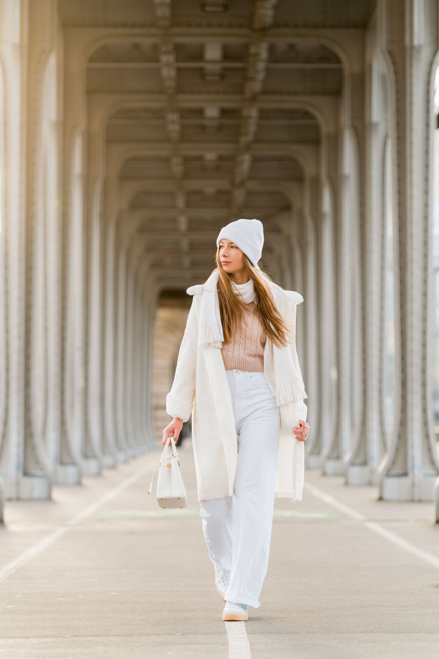 Winter fashion look captured in an elegant colonnade with white coat and beanie.