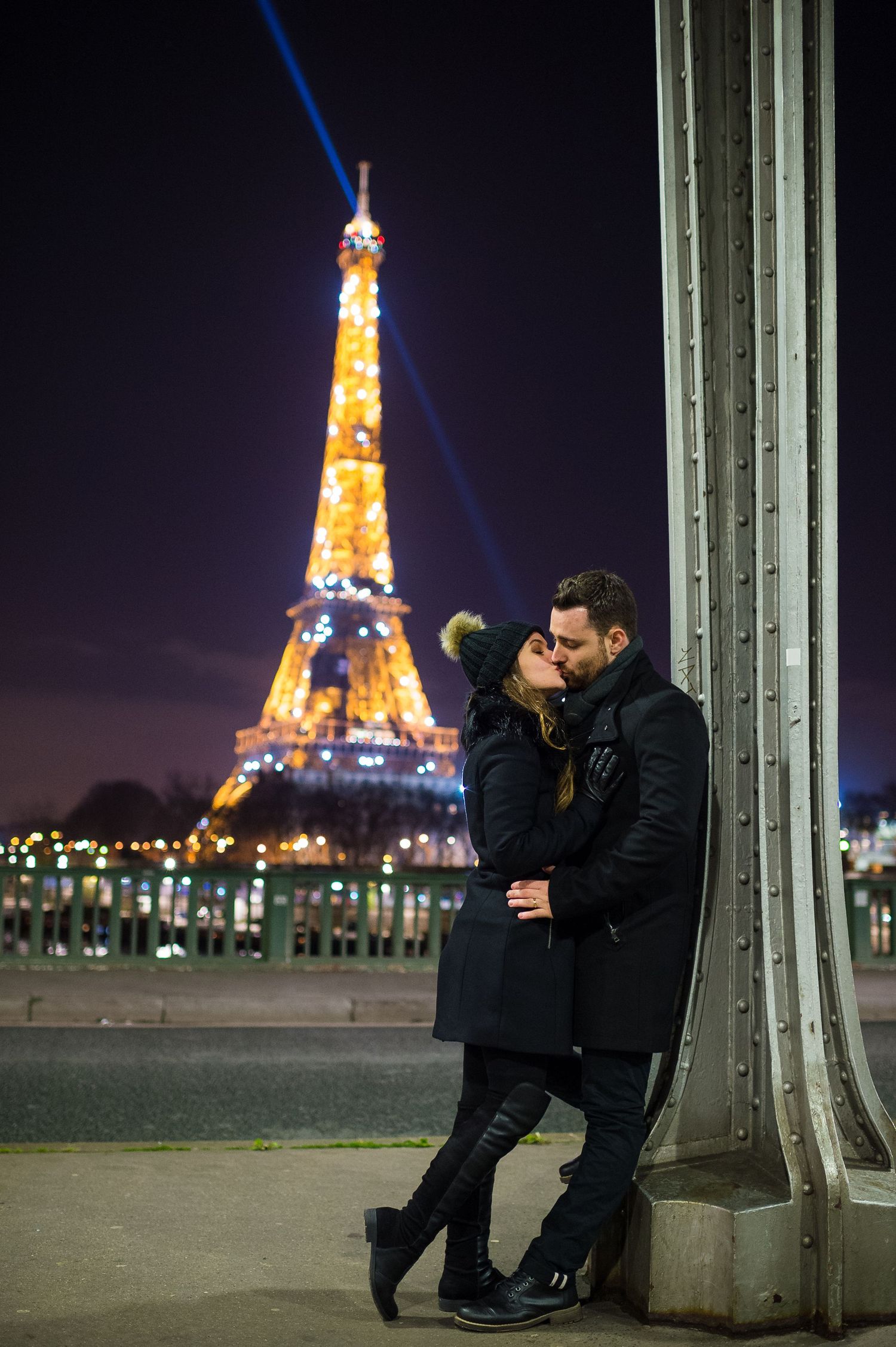 A couple enjoys a romantic evening by the illuminated Eiffel Tower in Paris, silhouetted against a dark night sky.