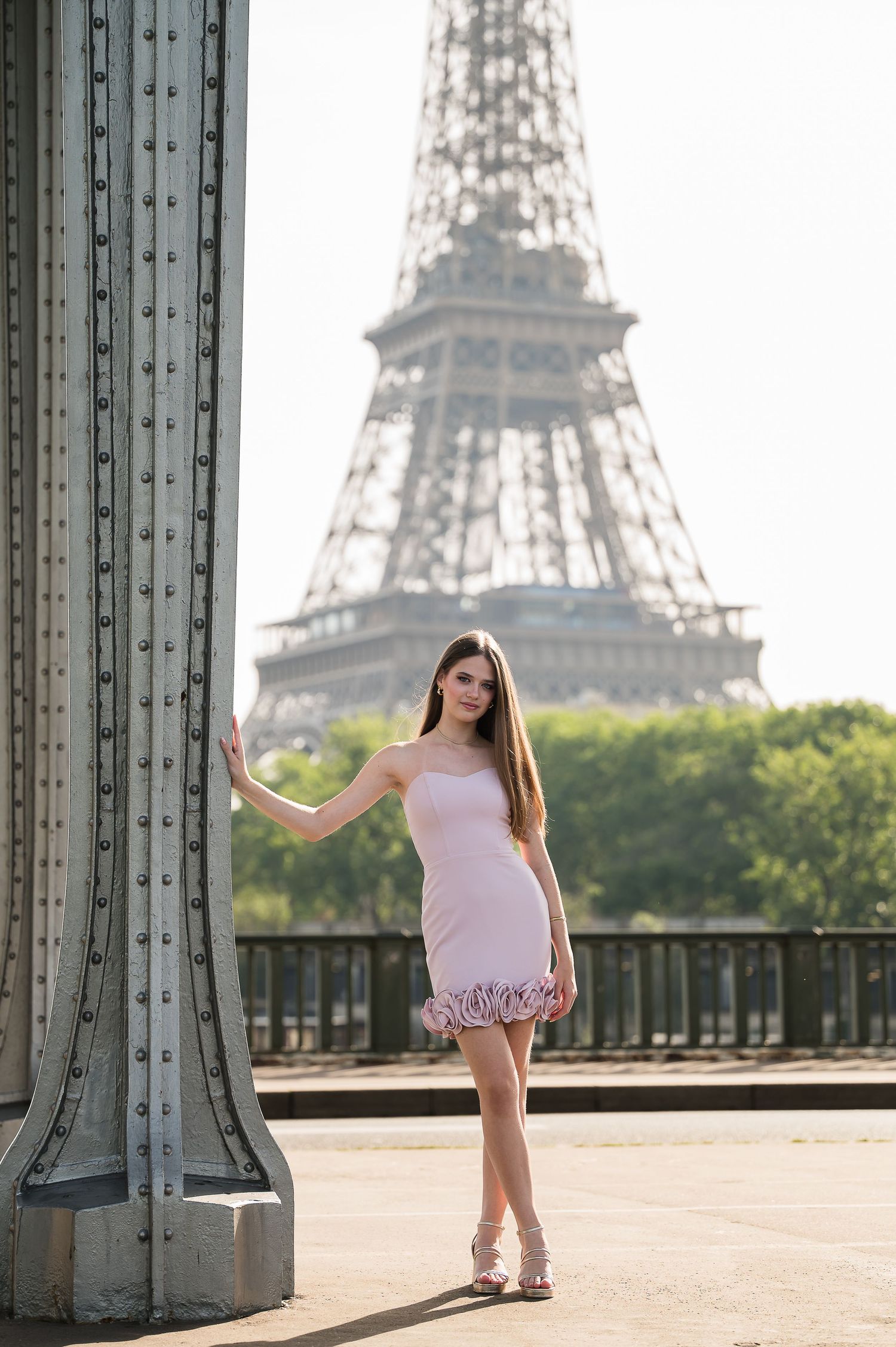 Young woman in pink dress posing near Eiffel Tower, Paris, on a sunny day.