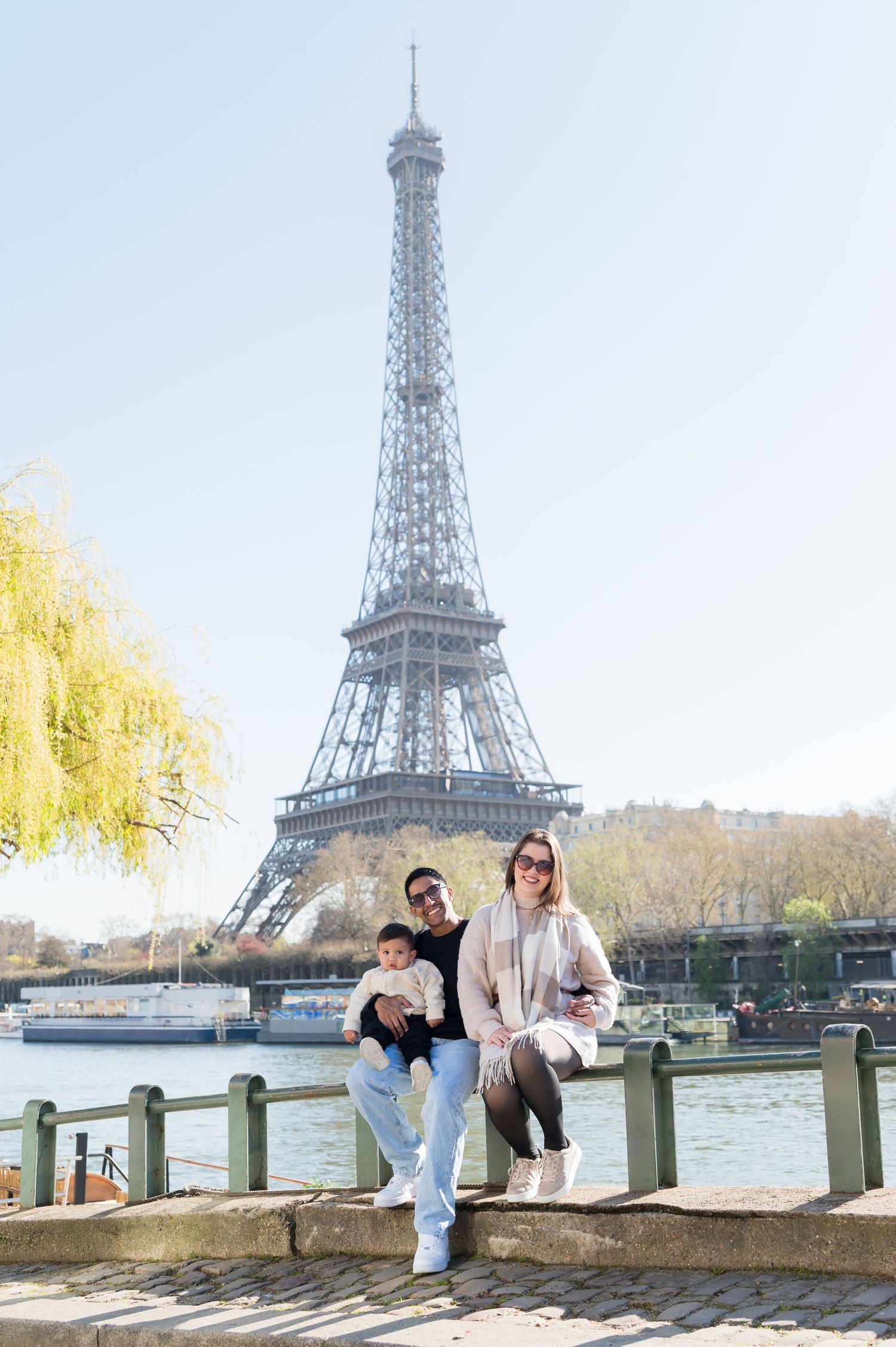 Family posing in front of the Eiffel Tower in Paris, France, on a sunny day by the Seine River.