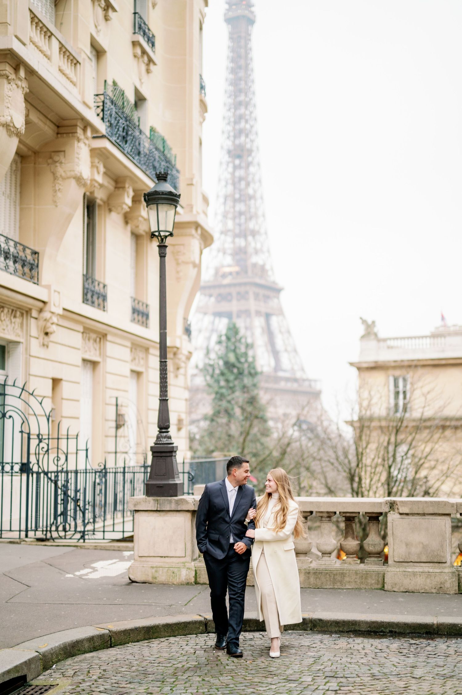 Elegant couple sharing a moment on cobblestone street with Eiffel Tower and historic buildings behind them.