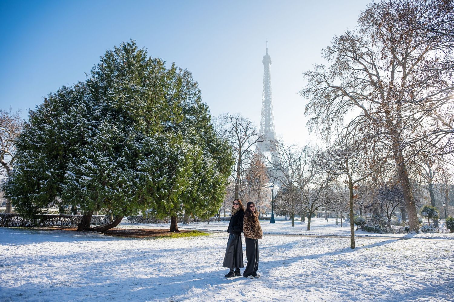 Snow covered park in Paris with the Eiffel Tower visible in the background on a winter day.