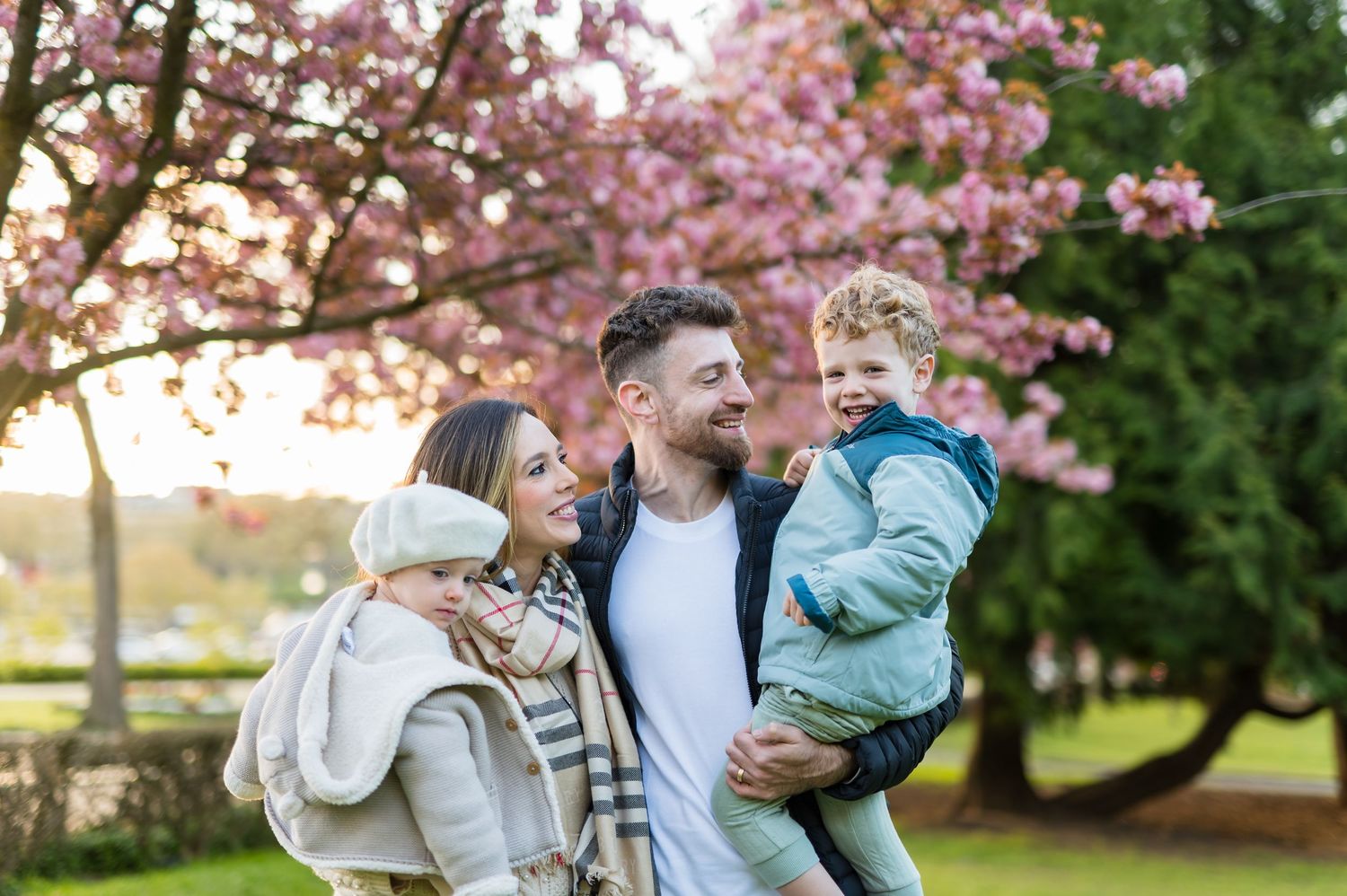 Happy family with two children enjoying spring outdoors near blooming pink cherry blossom trees.