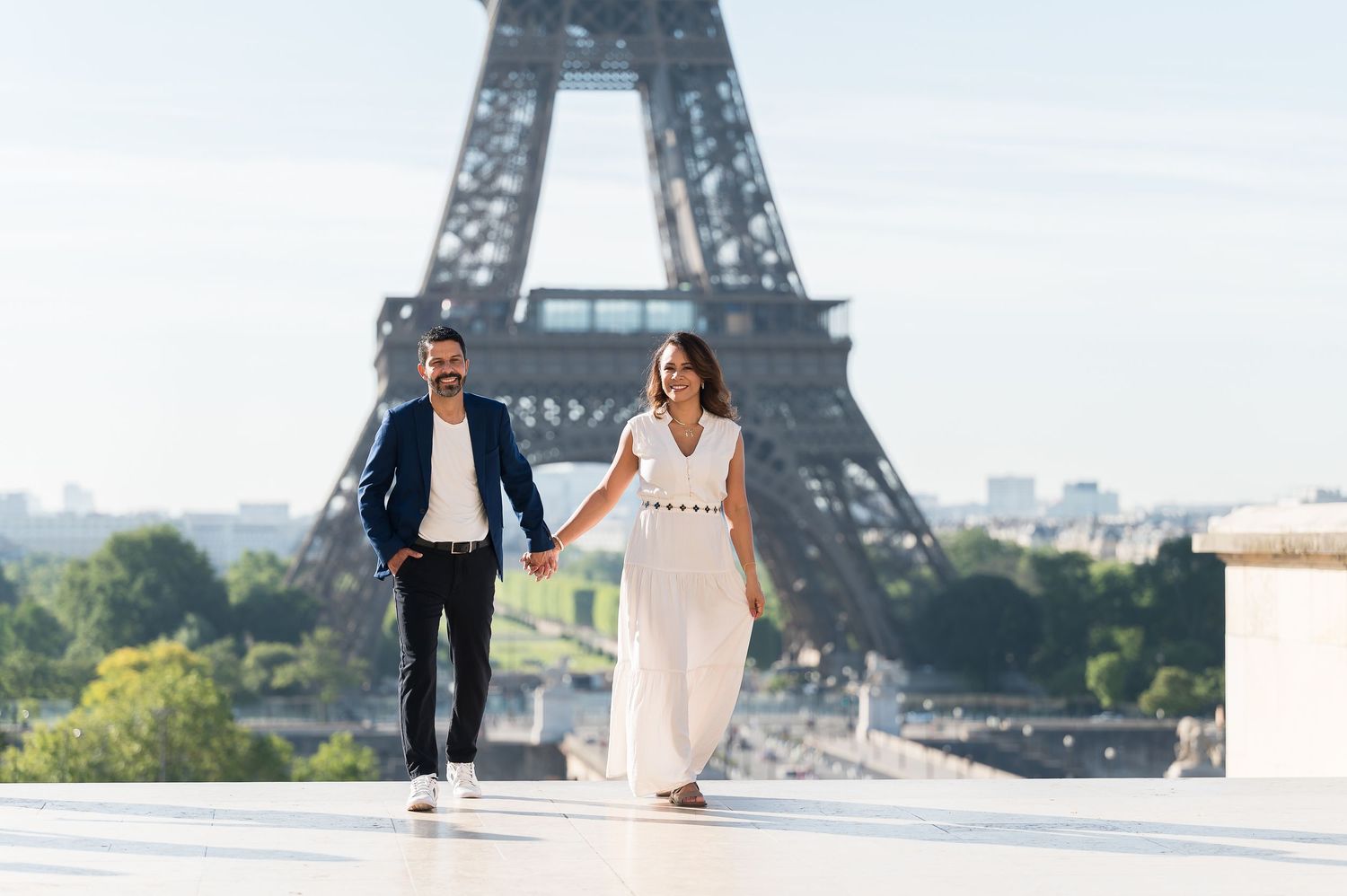 Couple holding hands walking at Trocadero with Eiffel Tower backdrop in Paris on a sunny day.