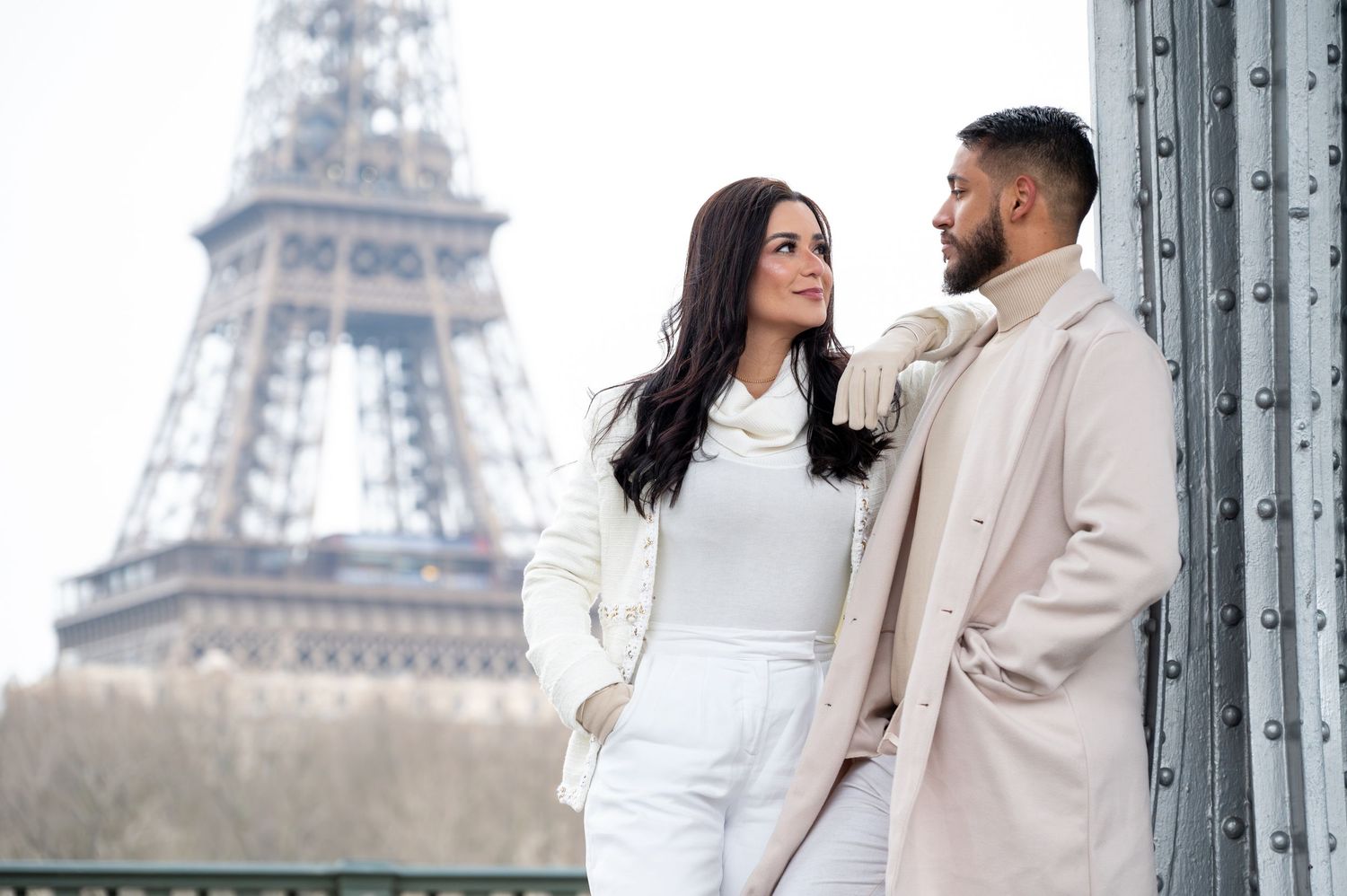 A couple in matching light-colored outfits shares a romantic moment near the Eiffel Tower in Paris.
