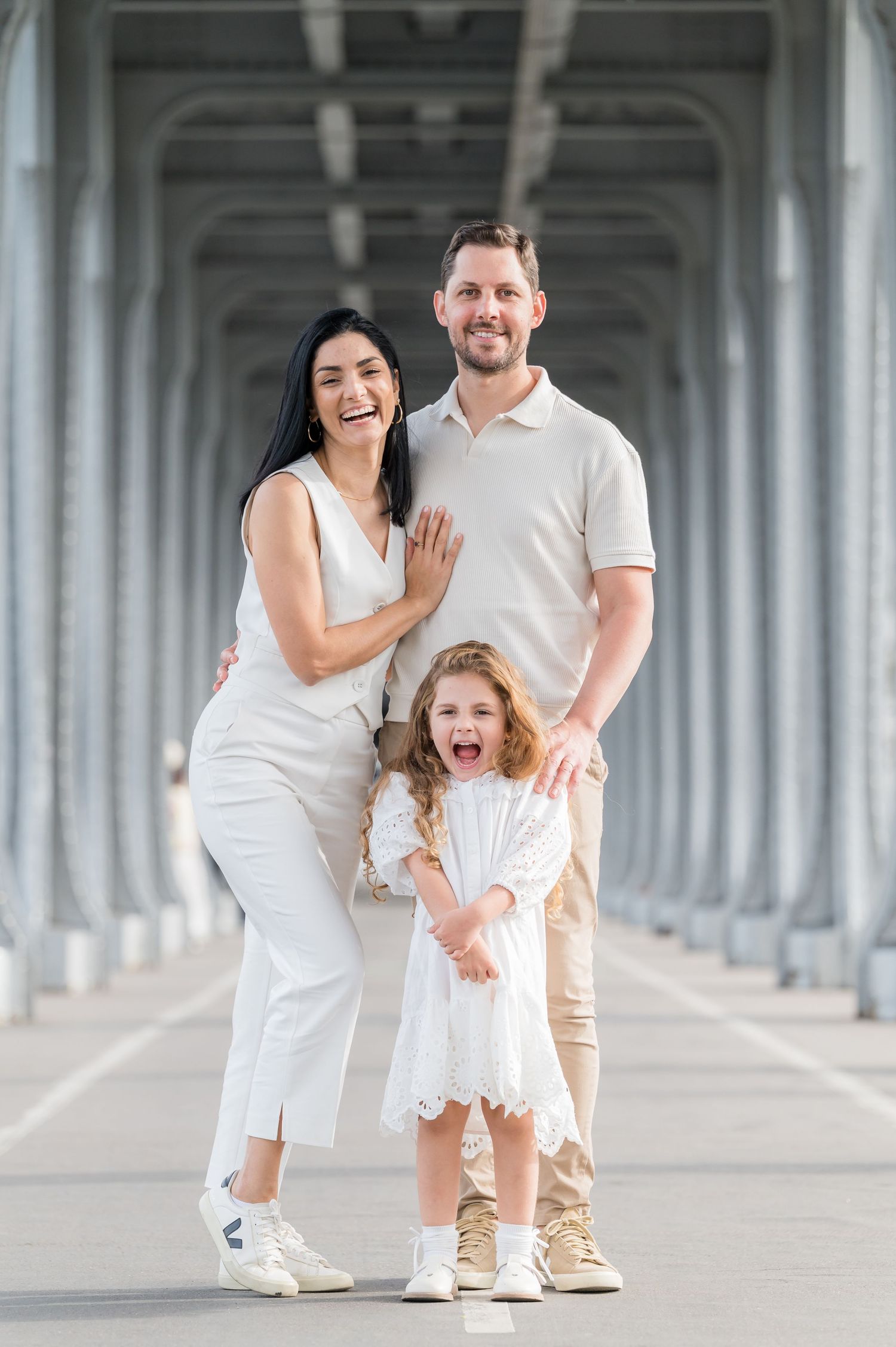 A family wearing coordinated white outfits poses together under a concrete bridge structure.