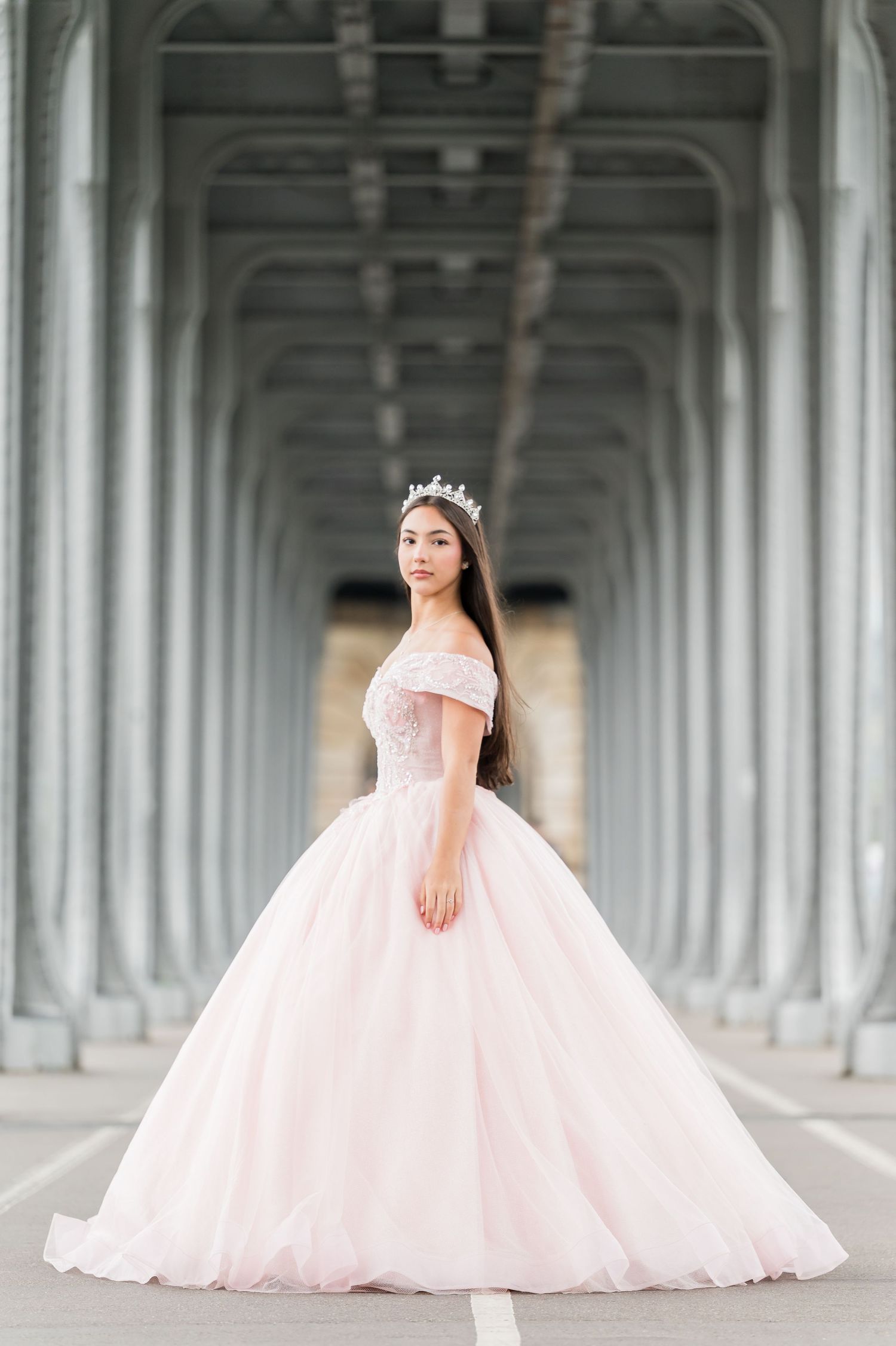 A bride in a flowing pink ballgown poses elegantly on the Bir Hakeim Bridge in Paris.