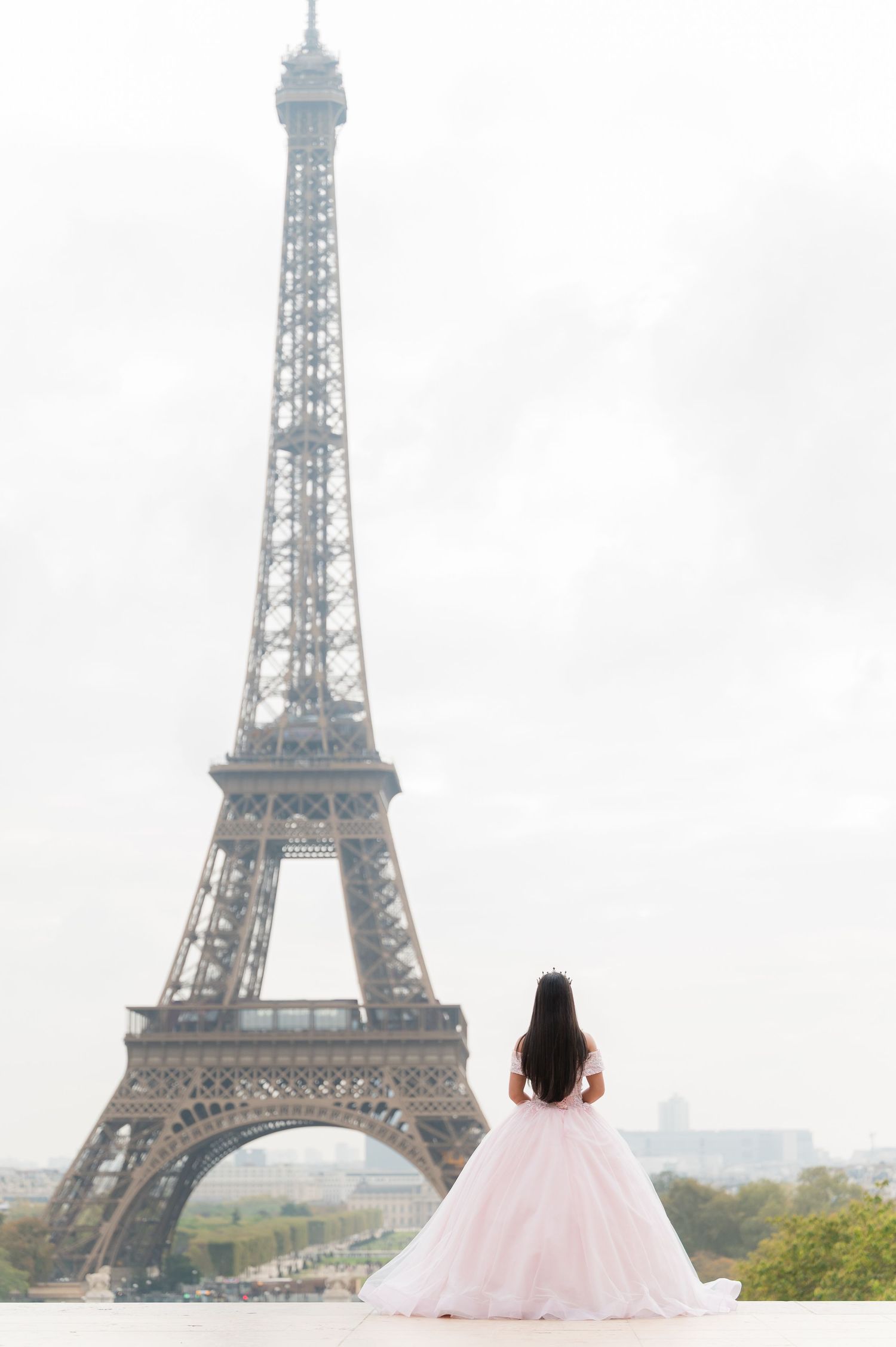 A woman in a pink ballgown poses in front of the iconic Eiffel Tower in Paris.