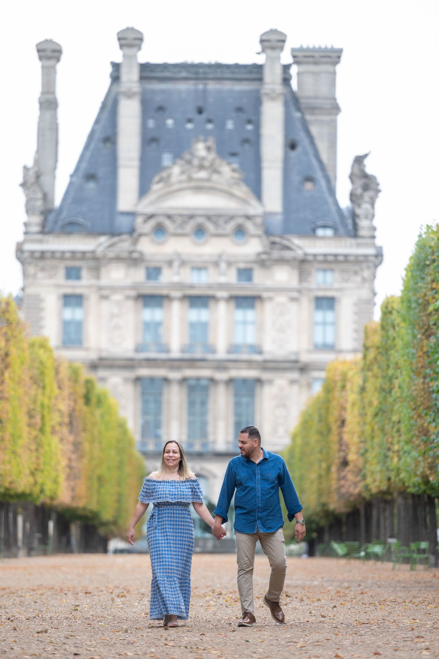 A couple strolling hand in hand along a tree-lined path at the Tuileries Garden in Paris.