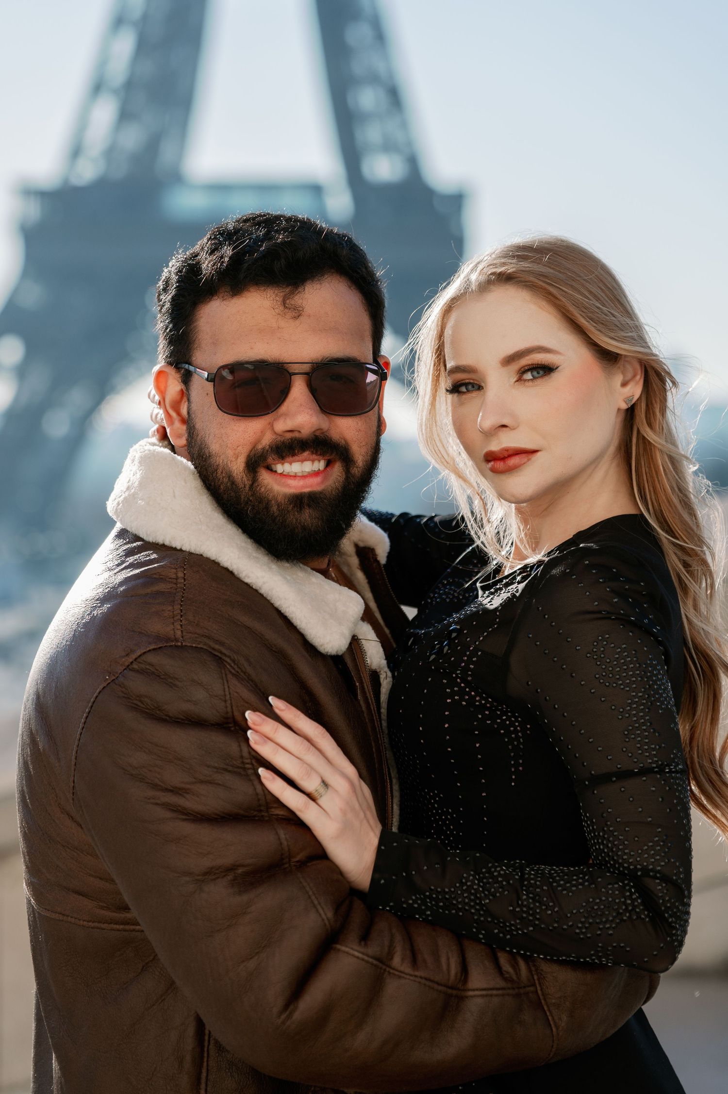 Couple in contrasting outfits pose together with Eiffel Tower backdrop in warm sunlight.