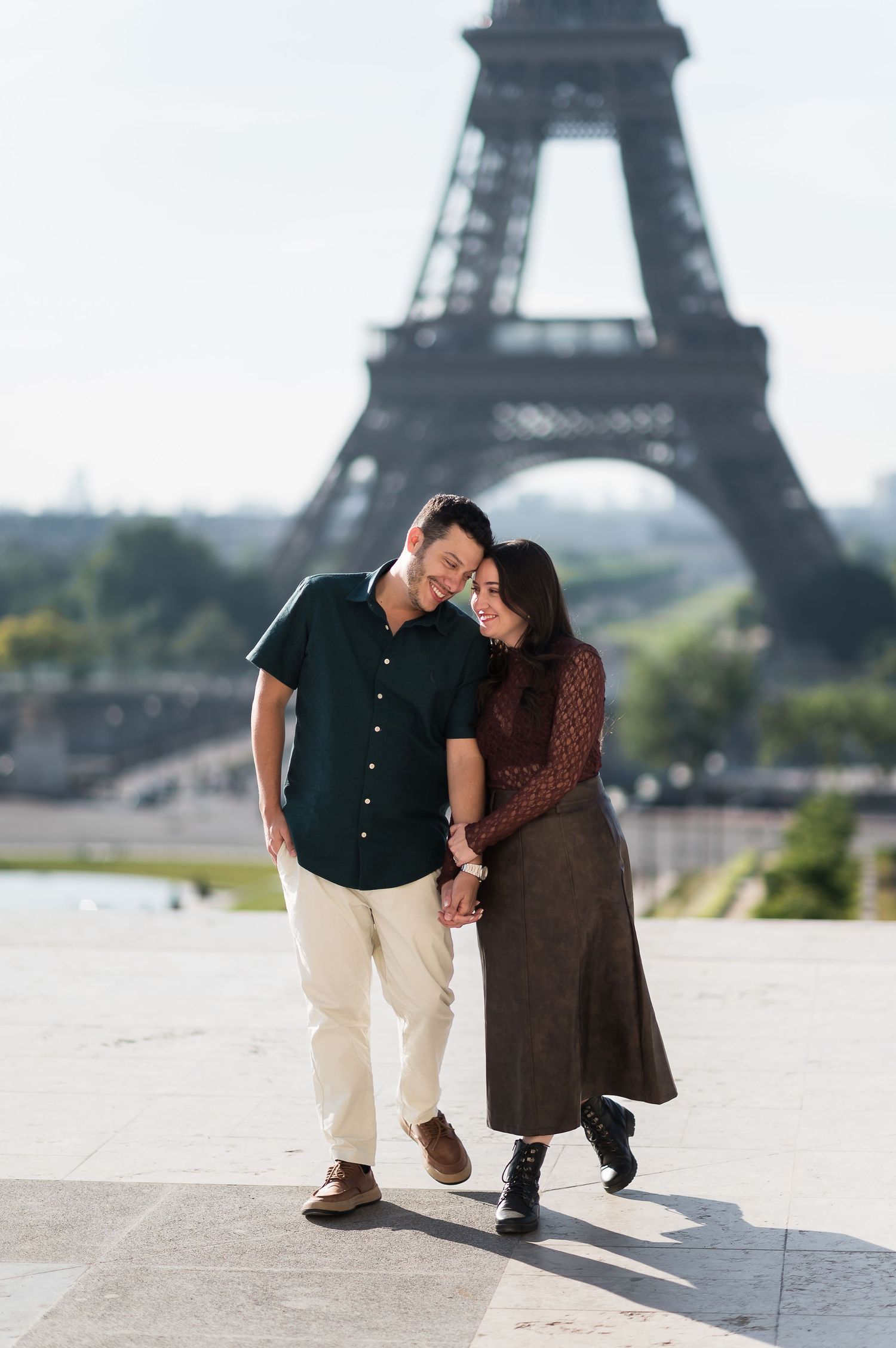 Couple holding hands and smiling in front of the Eiffel Tower in Paris, France.