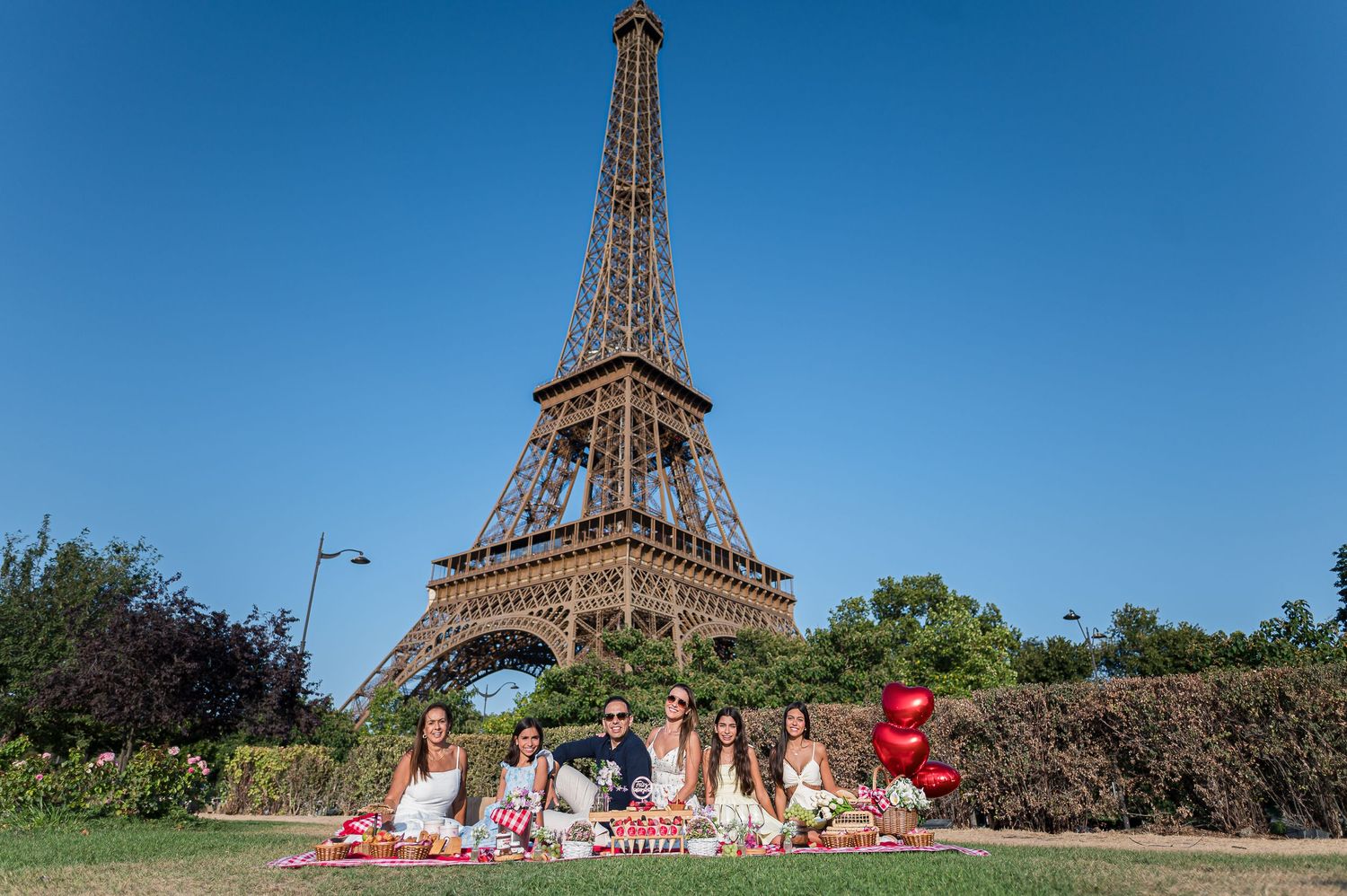 Group of friends enjoying a picnic on the grass in front of the Eiffel Tower in Paris on a sunny day.