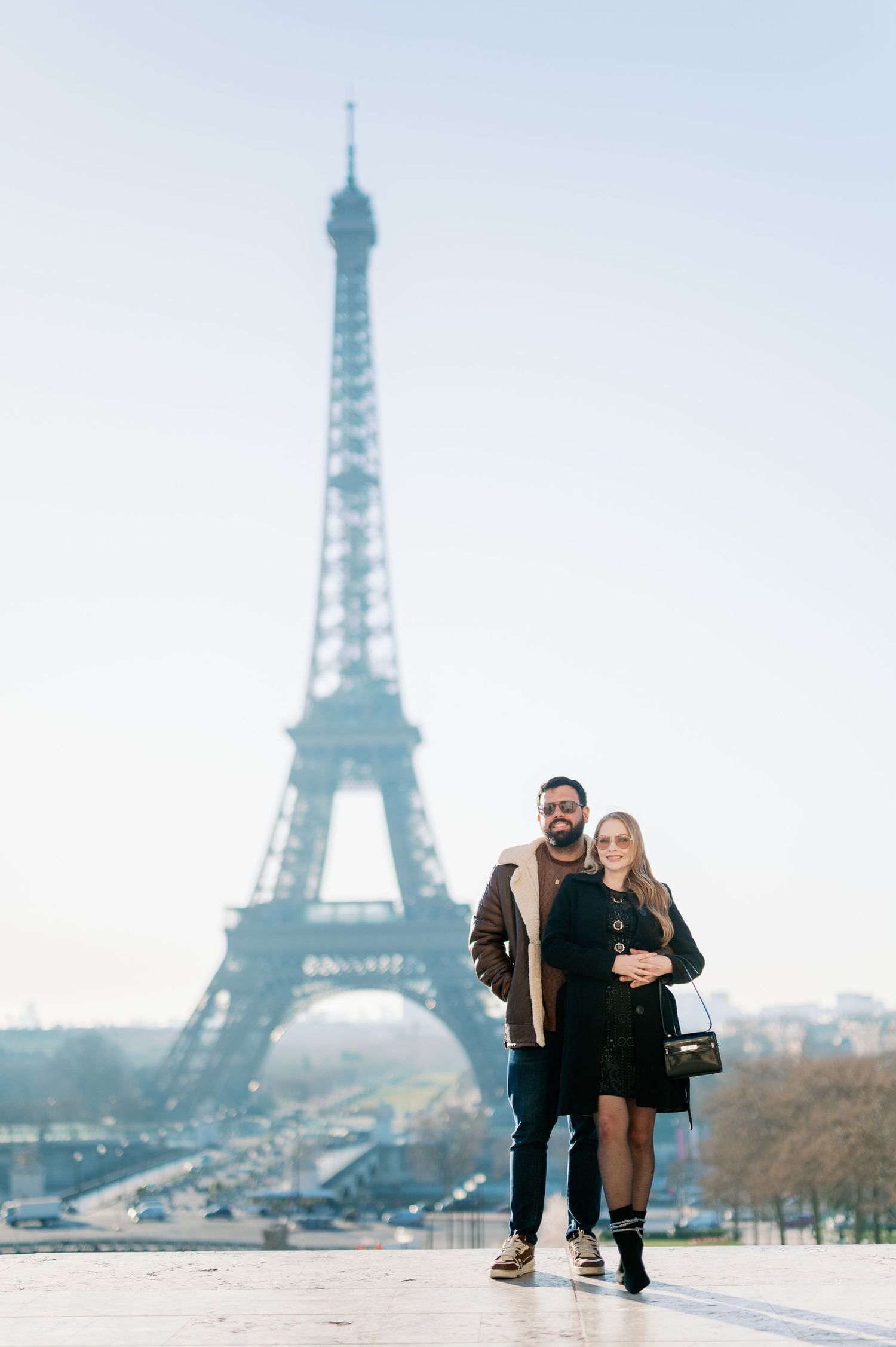 Couple standing close together against misty Eiffel Tower backdrop in Paris.
