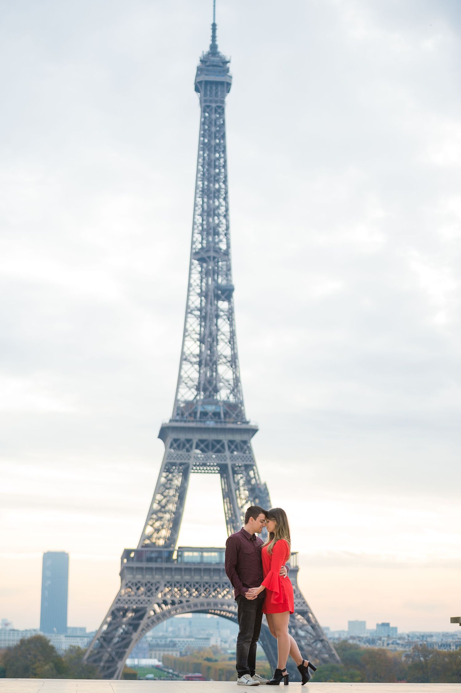 A romantic couple embraces in front of the iconic Eiffel Tower in Paris during sunset.