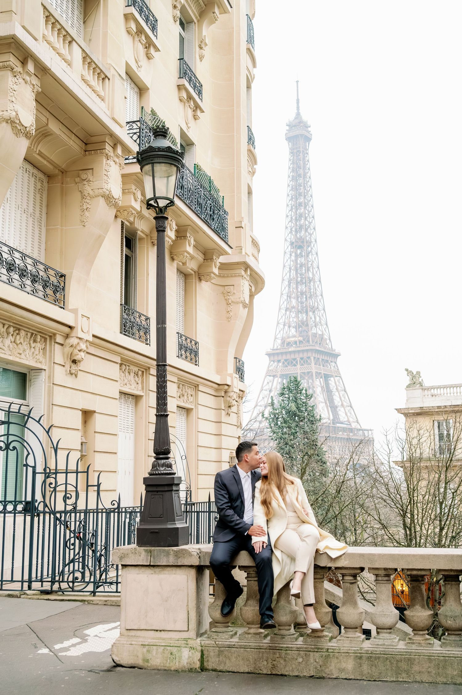 Romantic scene on a Parisian balcony with cream-colored buildings and Eiffel Tower in background.