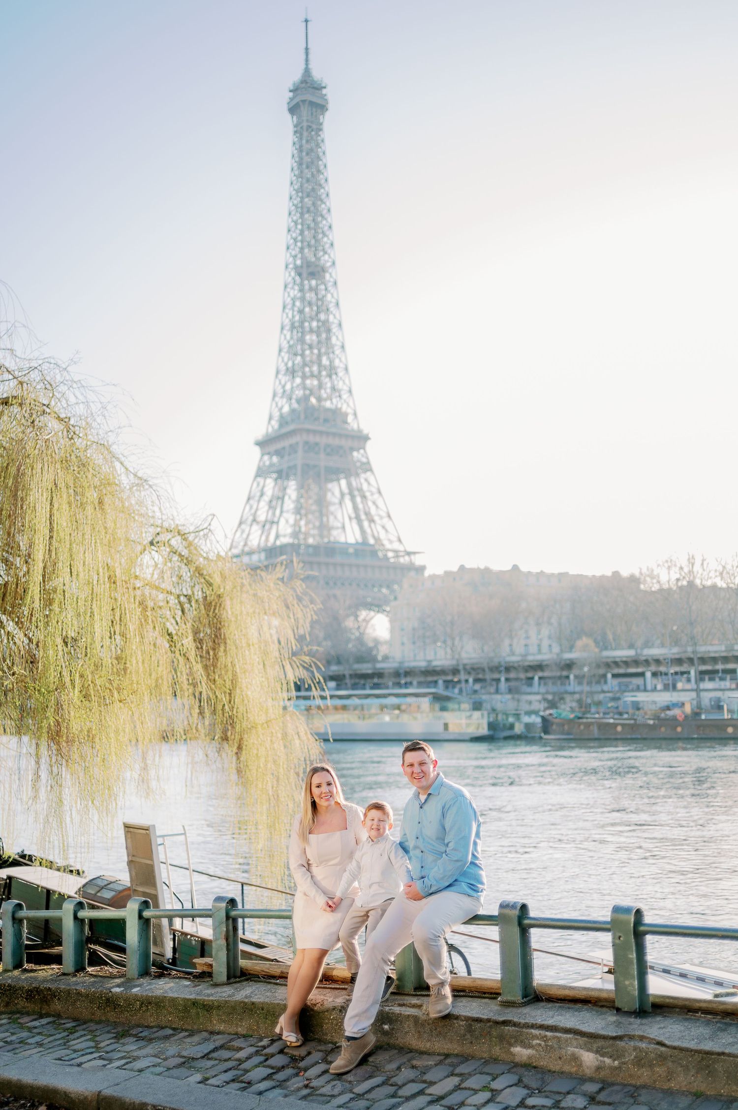 Family enjoying sunset moment by Seine River with Eiffel Tower in background.