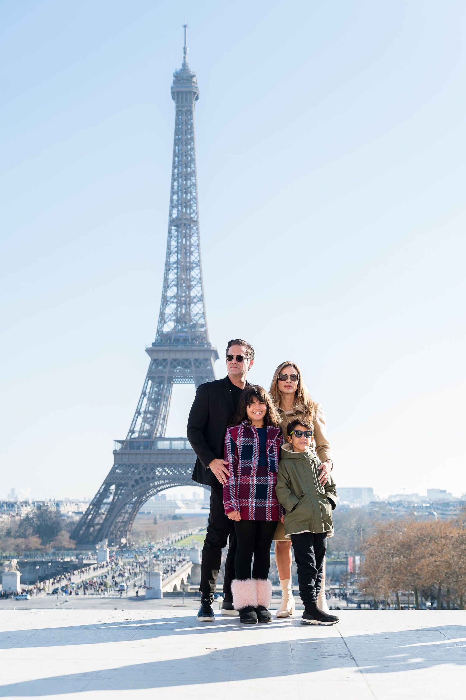 A family poses together on a sunny day with the iconic Eiffel Tower rising majestically in the background in Paris.