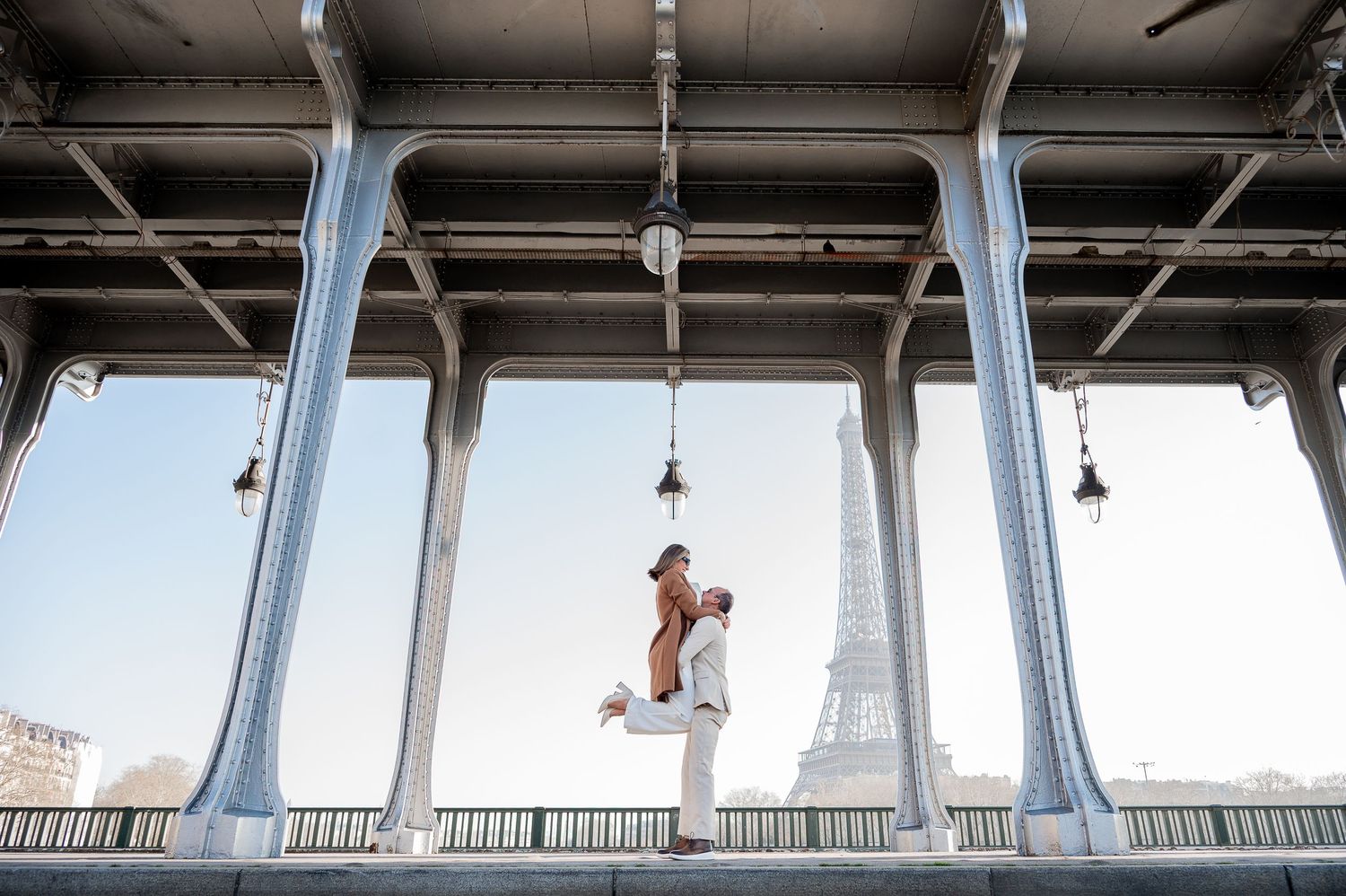 A couple shares a romantic dance under architectural columns with the Eiffel Tower visible in the distance.