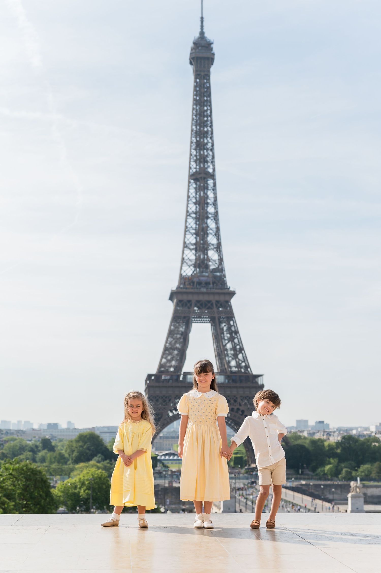Three children in yellow outfits enjoy a summer morning at the iconic Trocadero Plaza with Eiffel Tower backdrop in Paris.