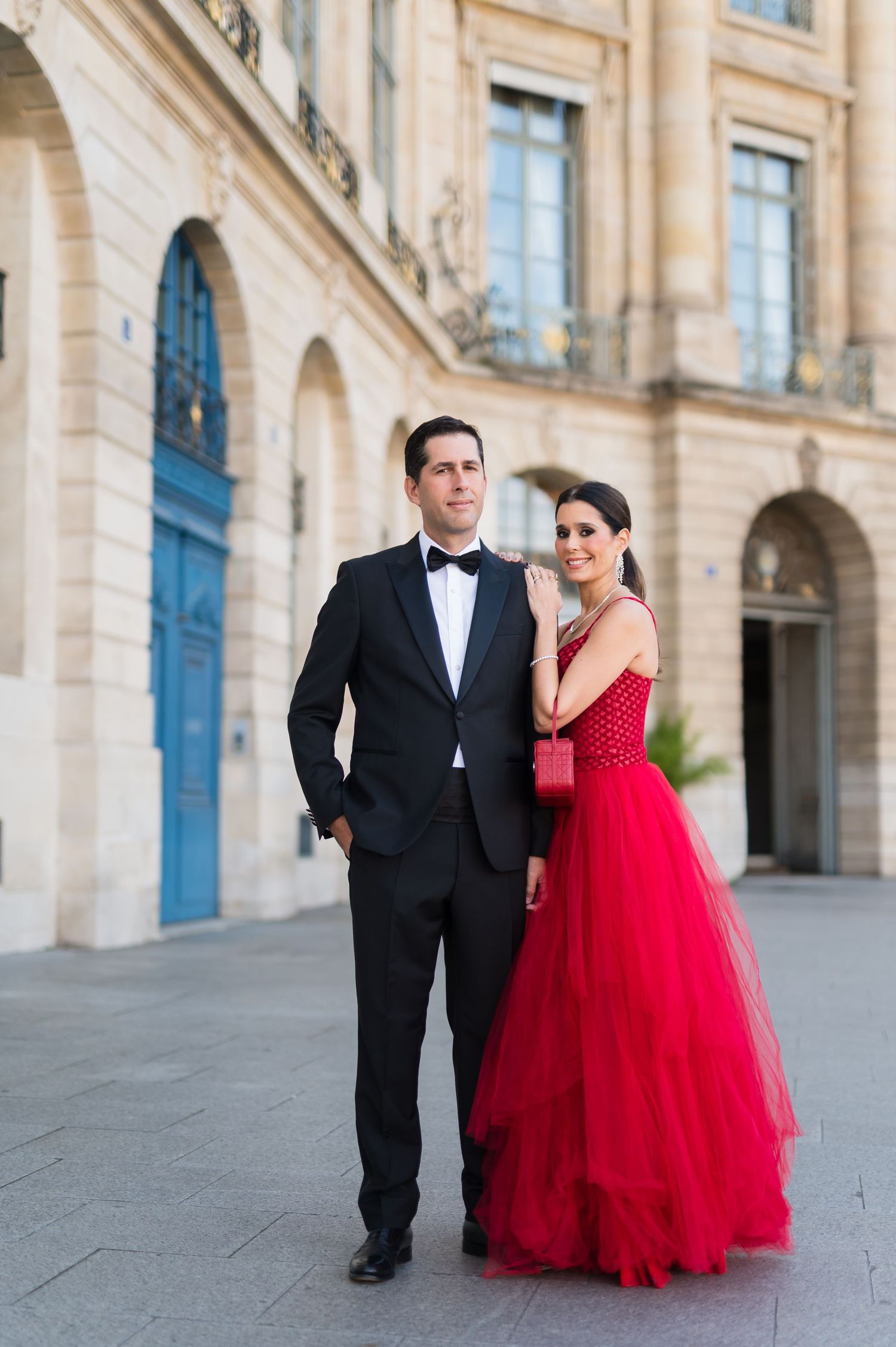Elegant couple posing in Paris, man in black tuxedo and woman in stunning red ball gown, outside classic French architecture.