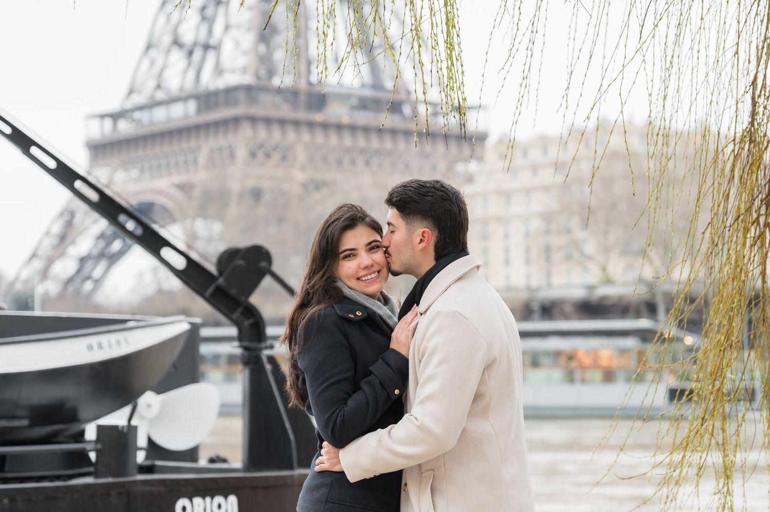 Romantic couple embracing near the Eiffel Tower in Paris, France on a cloudy day.