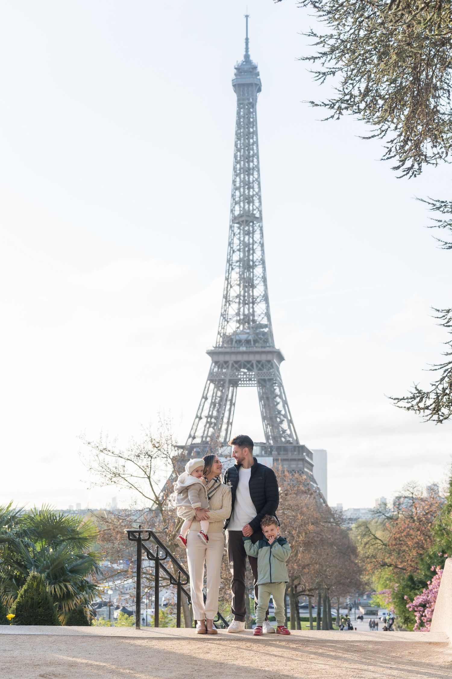 Family of three posing in front of the Eiffel Tower in Paris on a sunny day.
