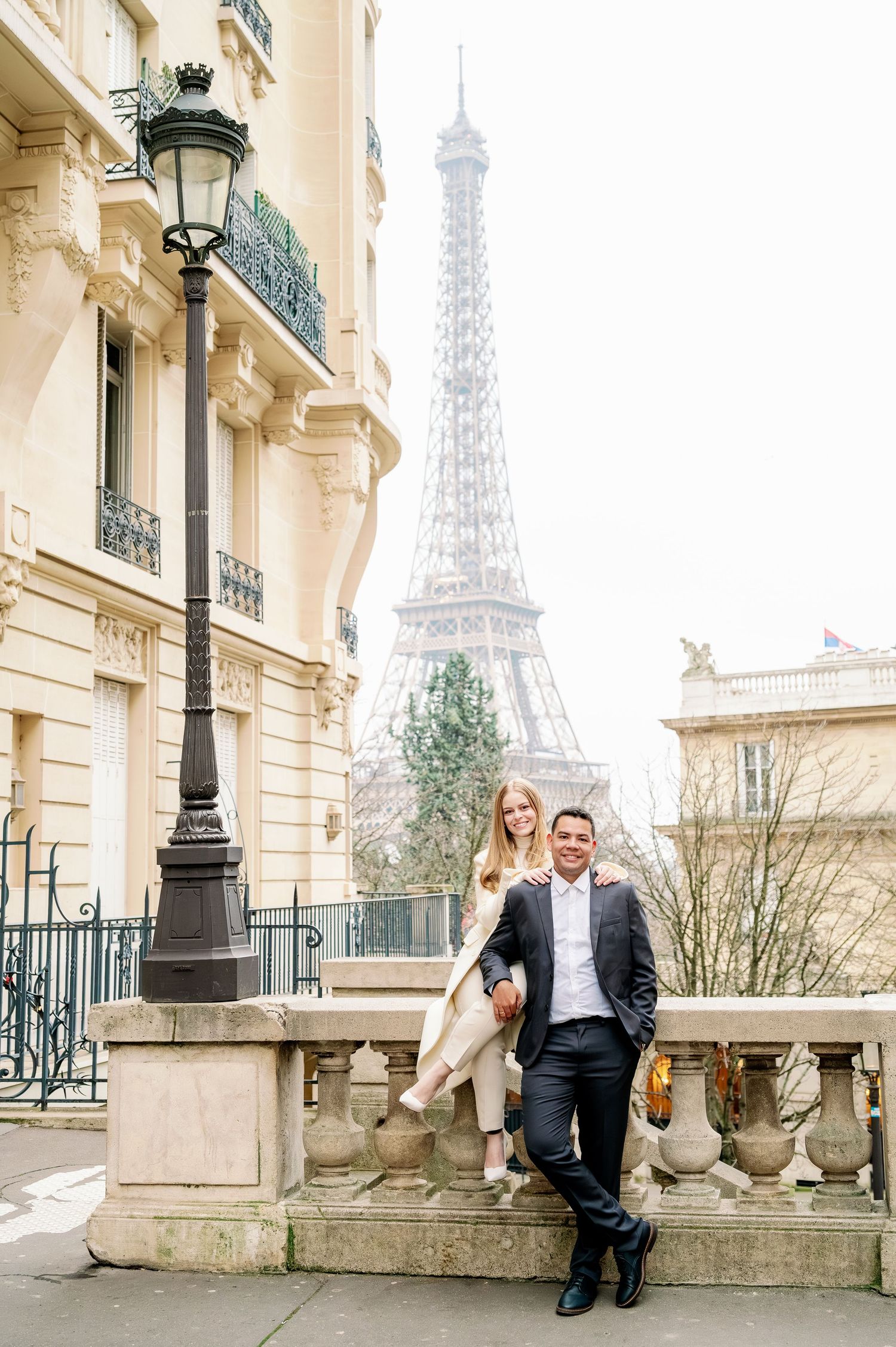 Elegant couple poses on historic Parisian balcony with Eiffel Tower view.
