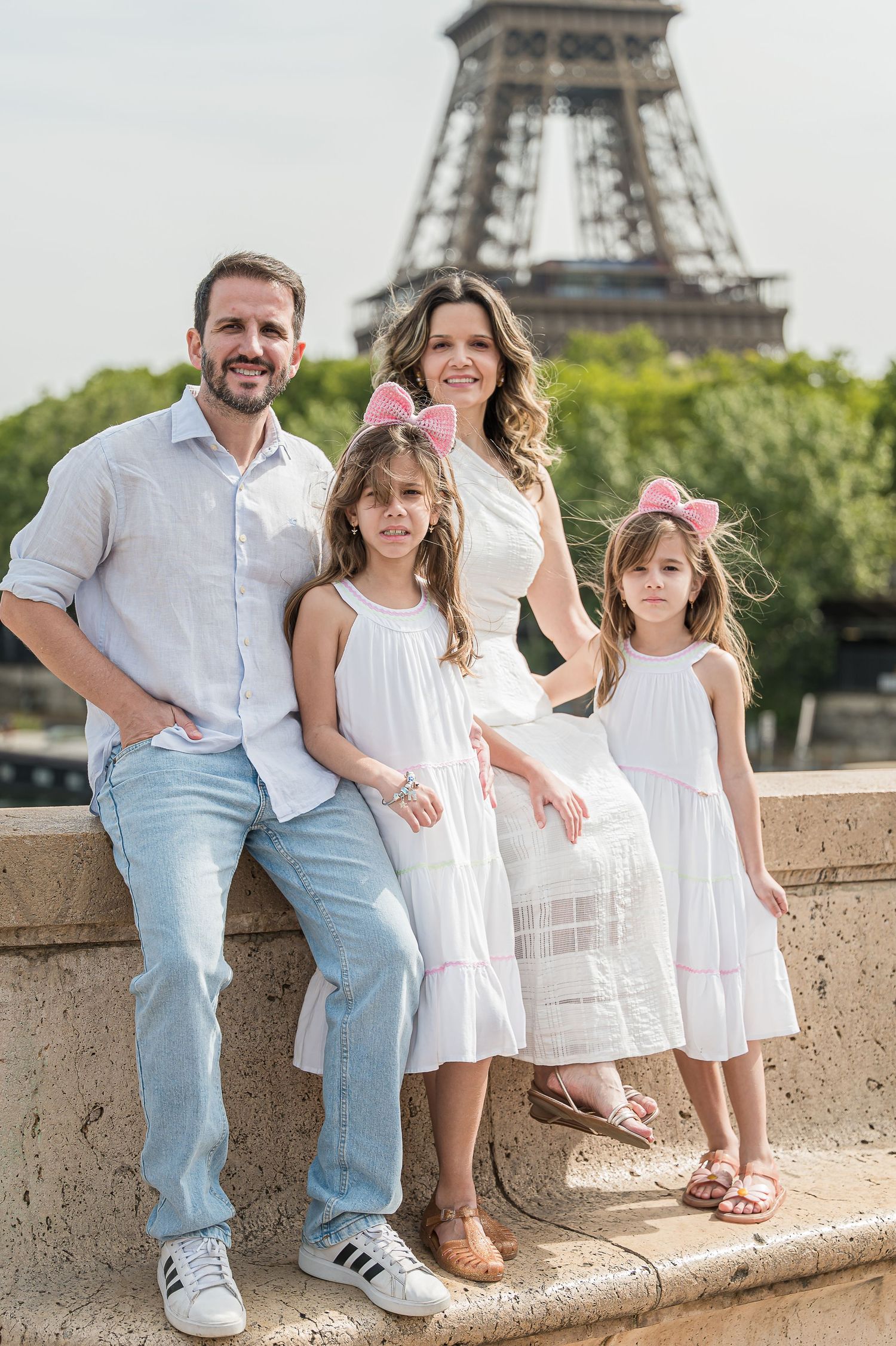 Family of four posing in front of the Eiffel Tower in Paris, wearing white outfits on a sunny day.