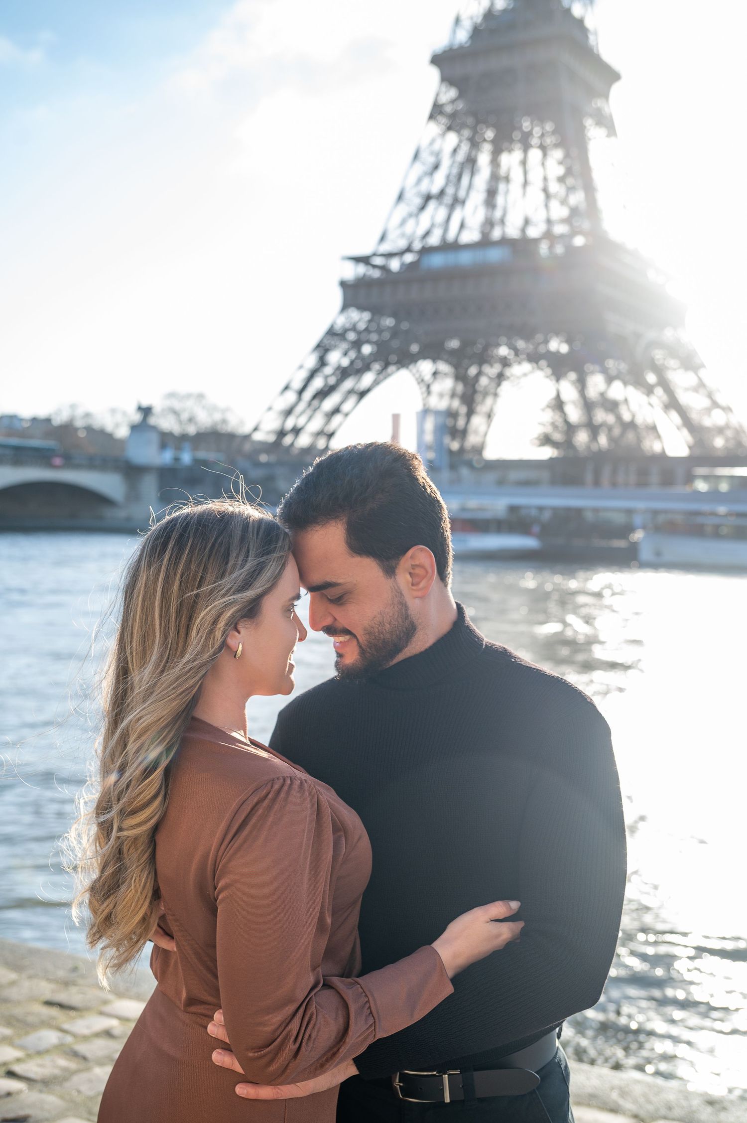 A romantic moment captured in front of the Eiffel Tower with sunlight streaming through the iconic structure.