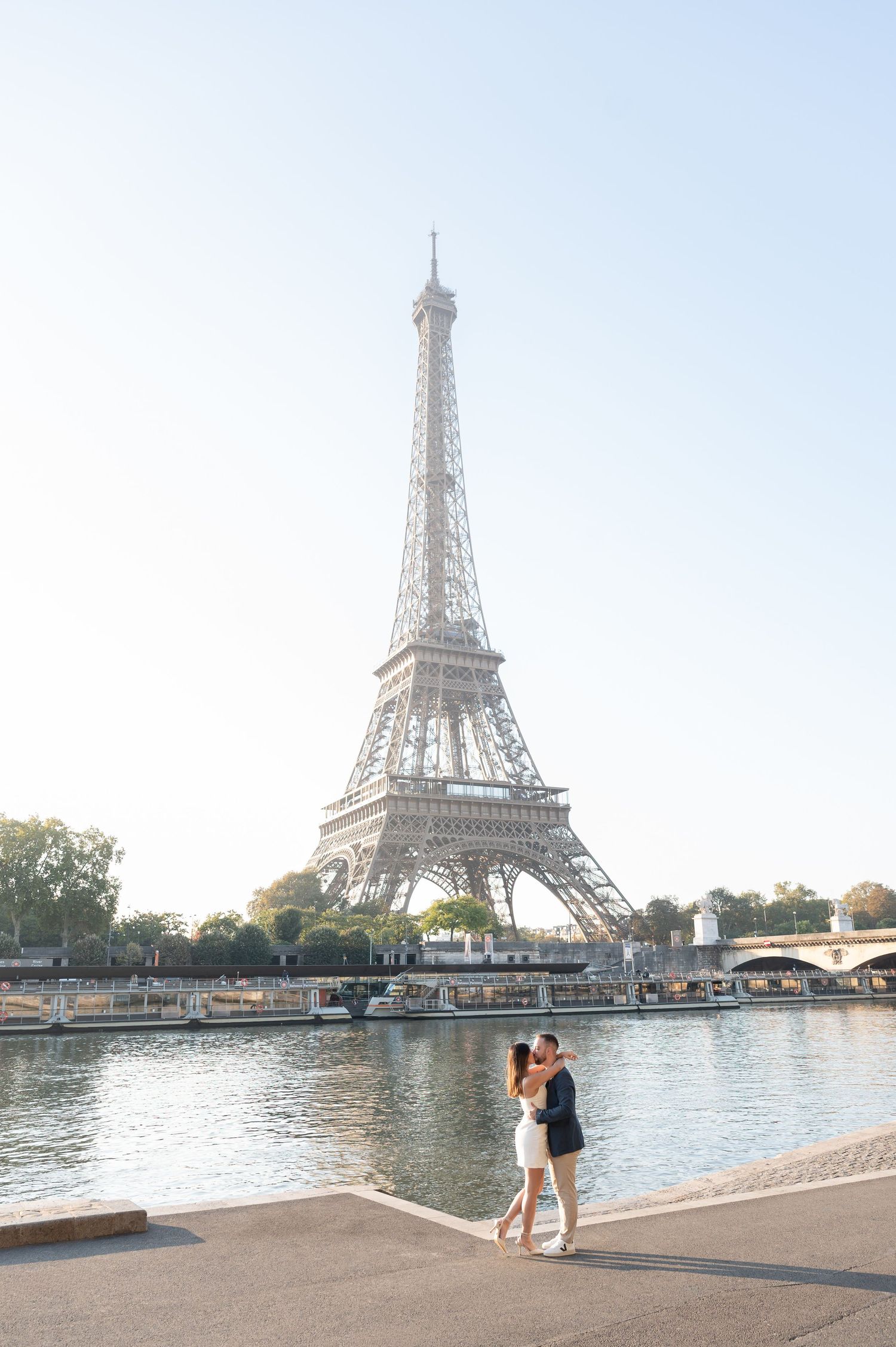 Couple kissing by the Seine River with the Eiffel Tower in the background on a sunny day in Paris.