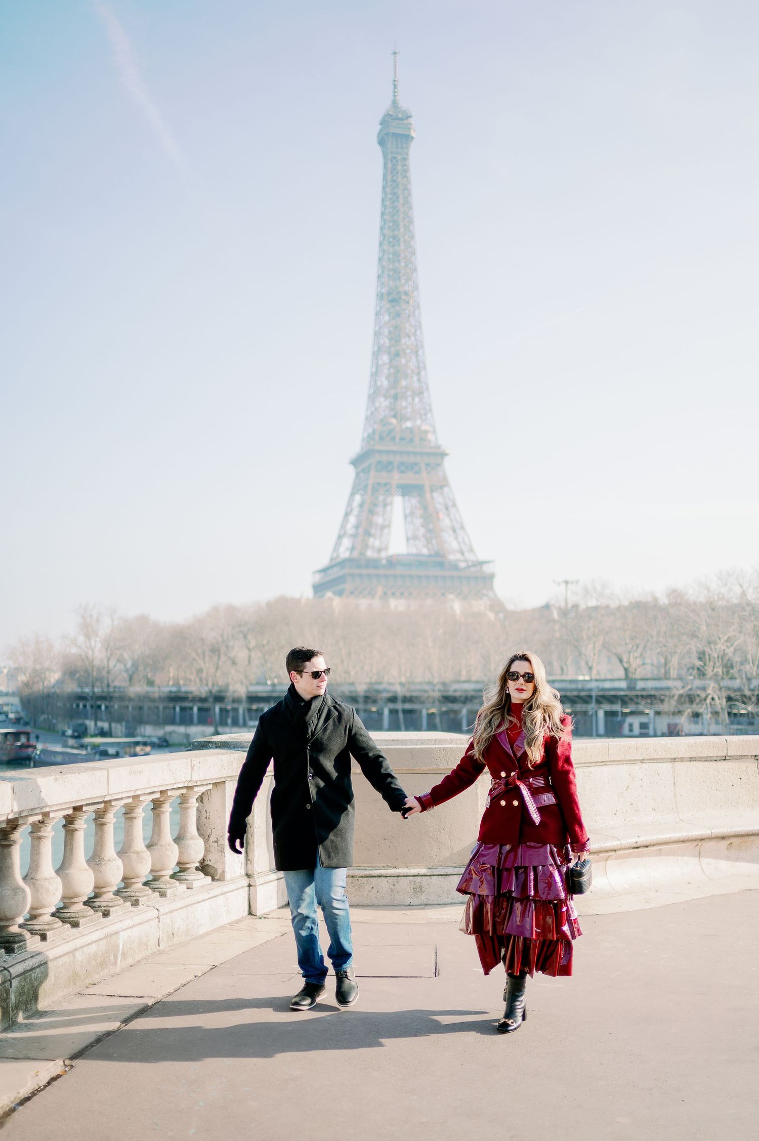 Couple walking hand in hand along Seine River with Eiffel Tower in background.