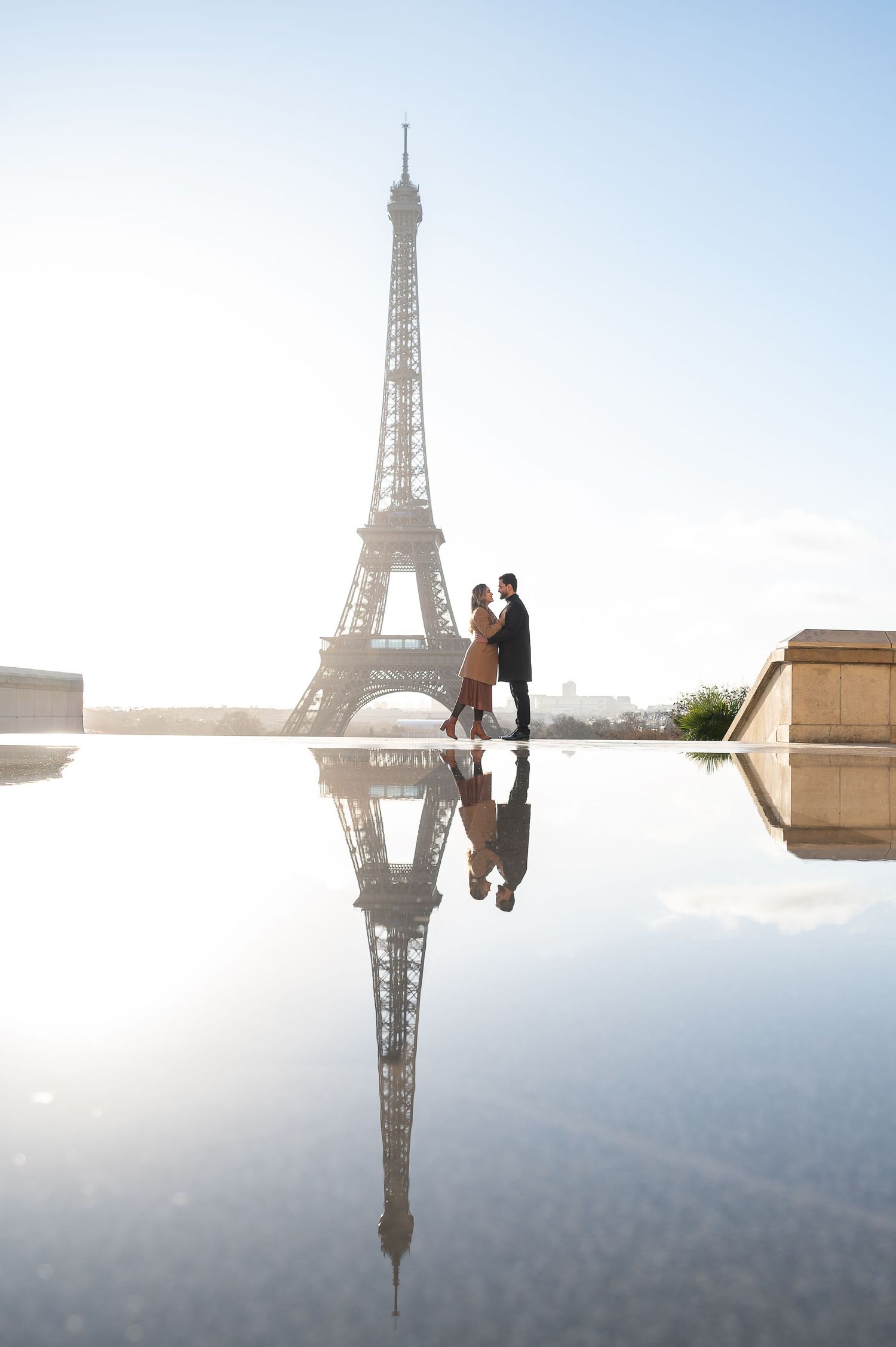 Silhouettes reflected in a puddle near the Eiffel Tower during golden hour in Paris.